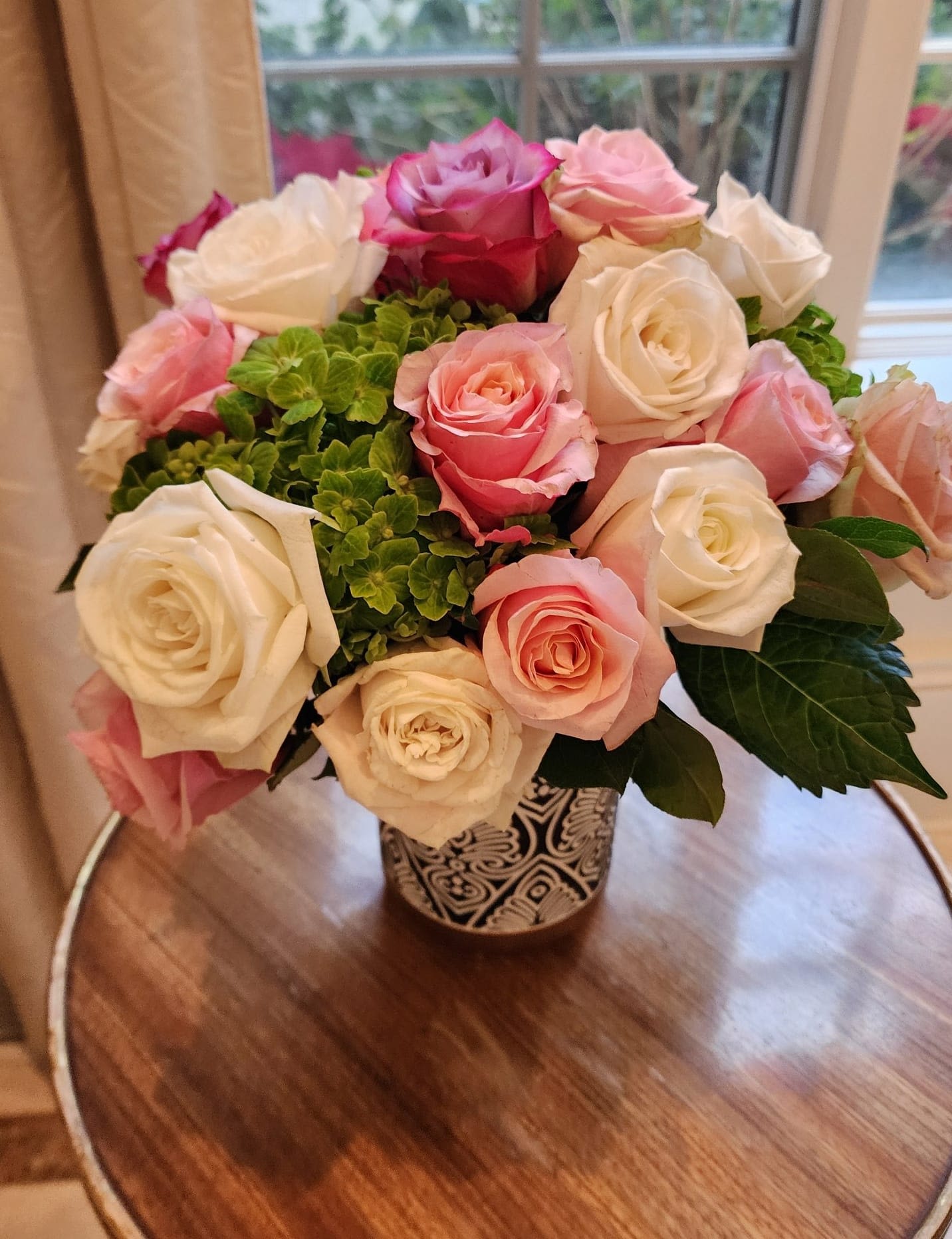 Compact arrangement of pink and white roses with green blooms in a patterned ceramic vase
