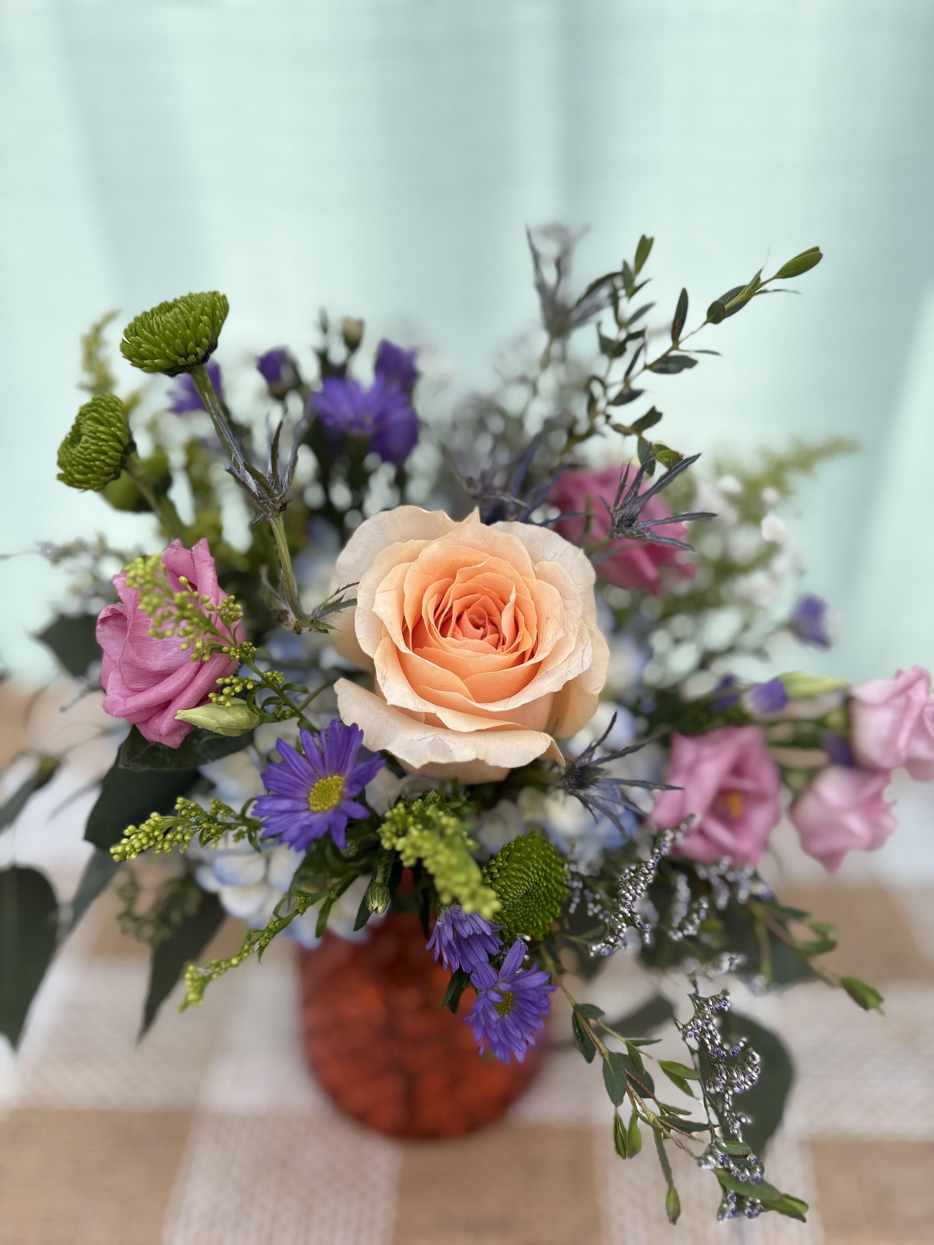 SUMMER WEATHER BOUQUET - A medium sized arrangement with purple blooms and an orange rose to remind you of sunny, summer weather