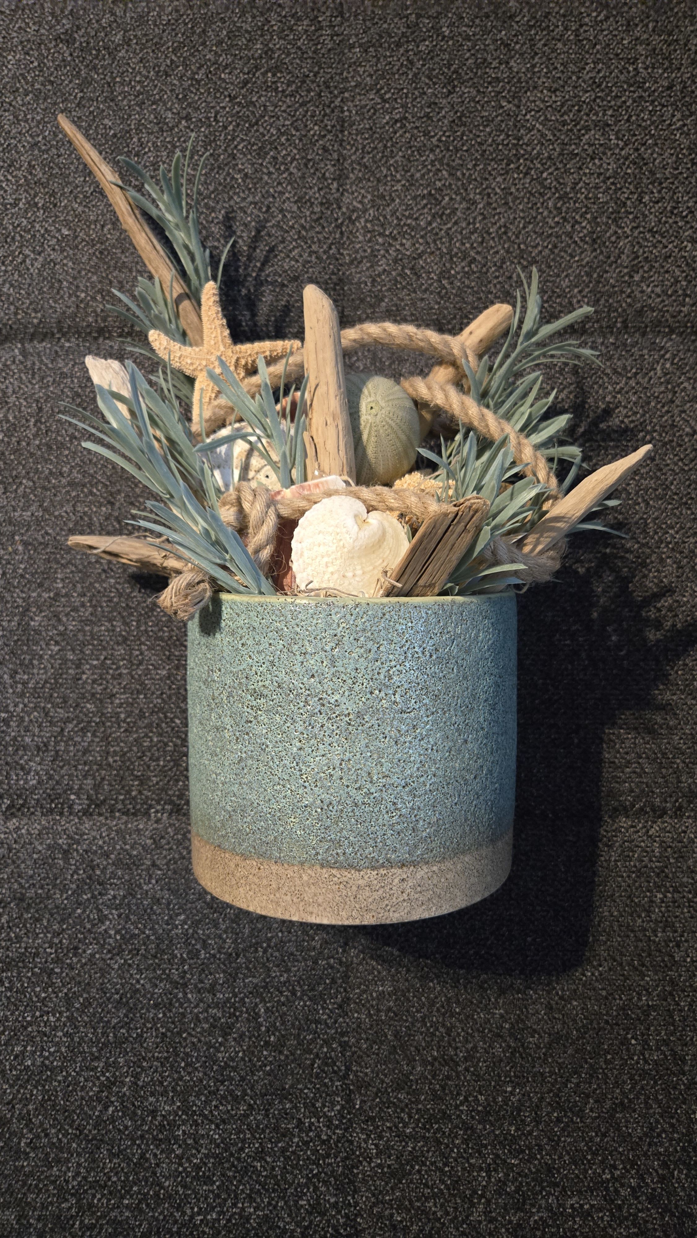 Coastal arrangement of driftwood, rope, and seashells in a blue ceramic pot with faux foliage.