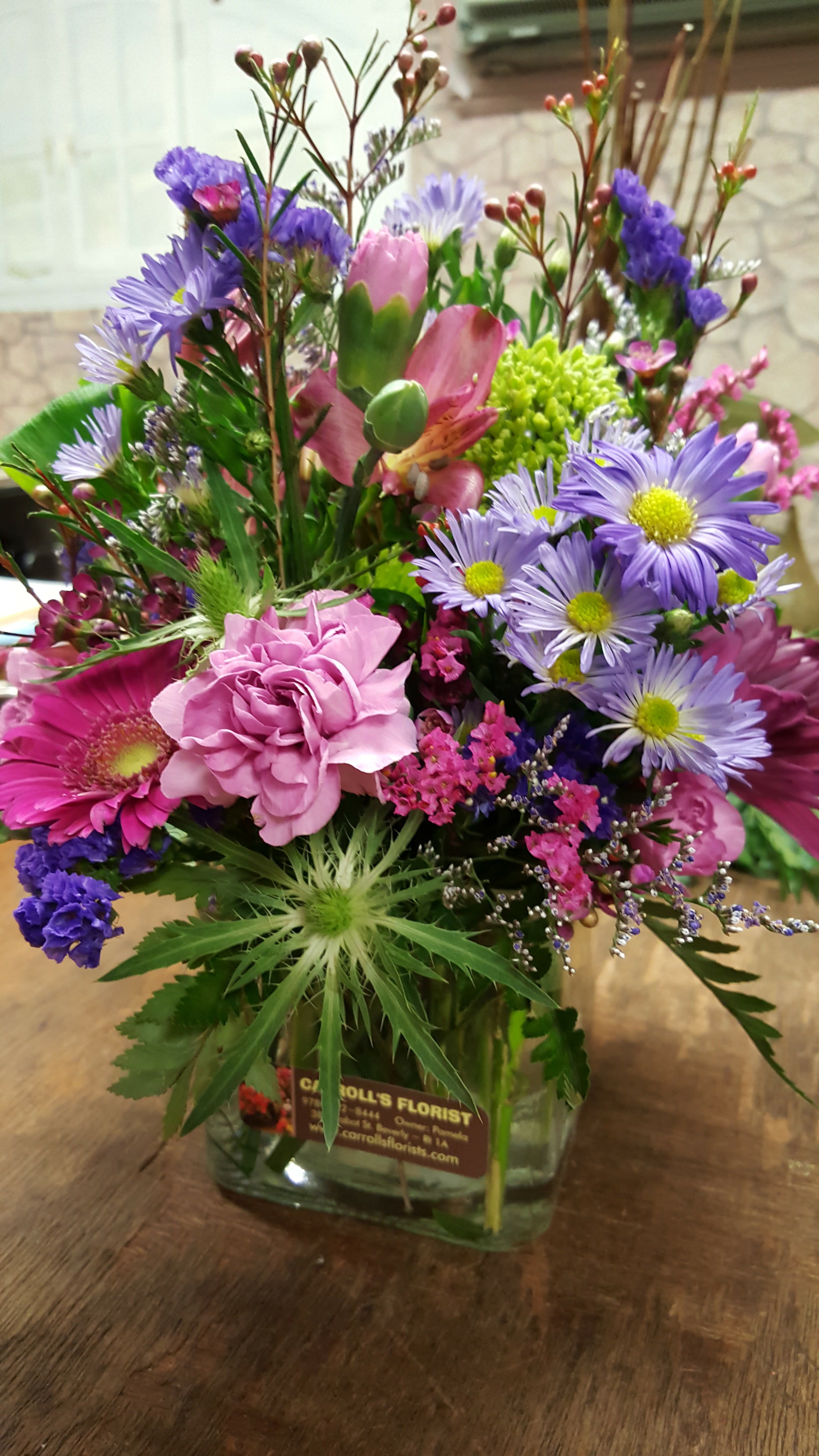 Mixed bouquet of purple daisies, pink carnation and gerbera in a clear glass cube vase