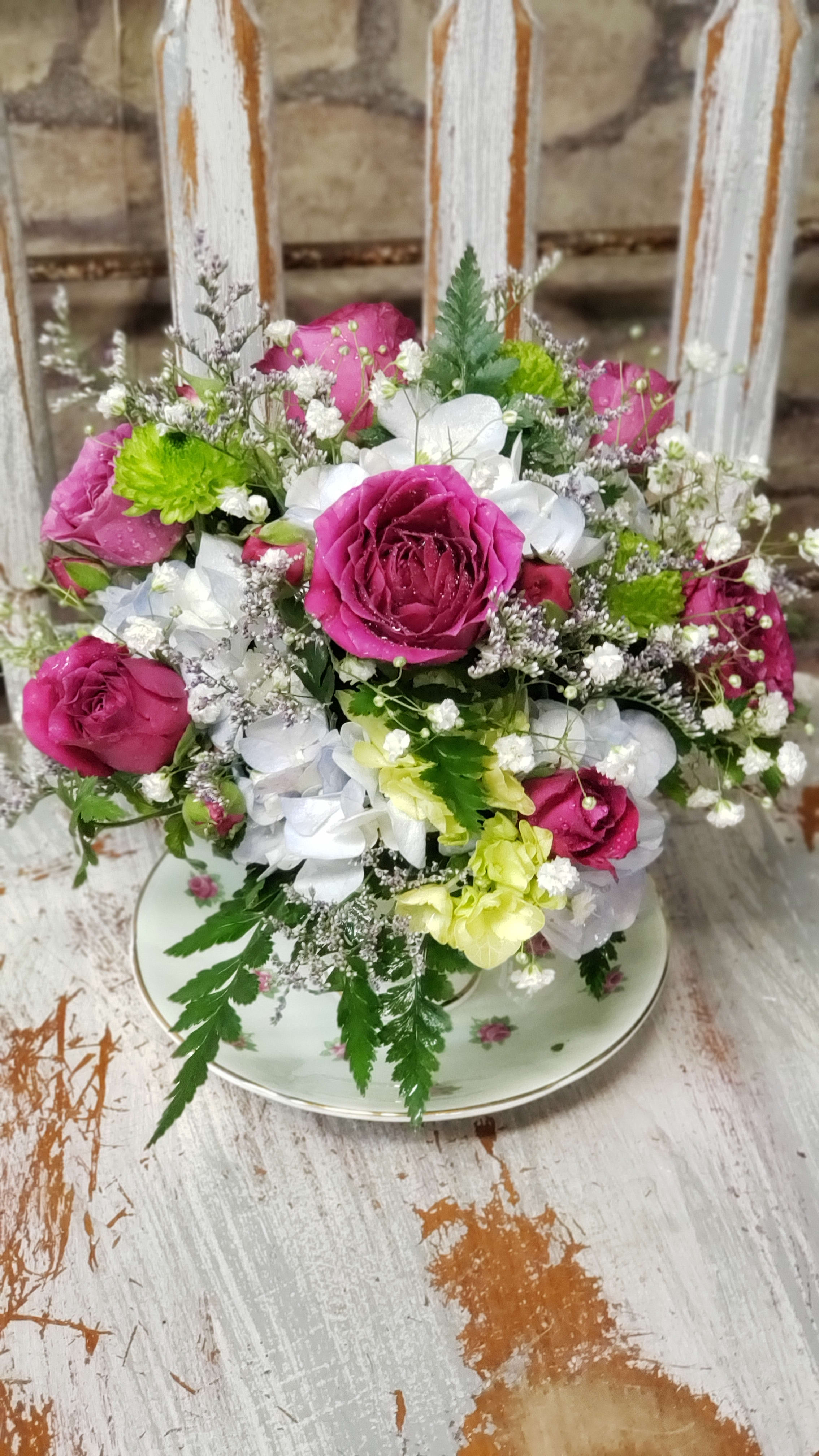Compact pink rose and white hydrangea arrangement in a floral teacup on a rustic table