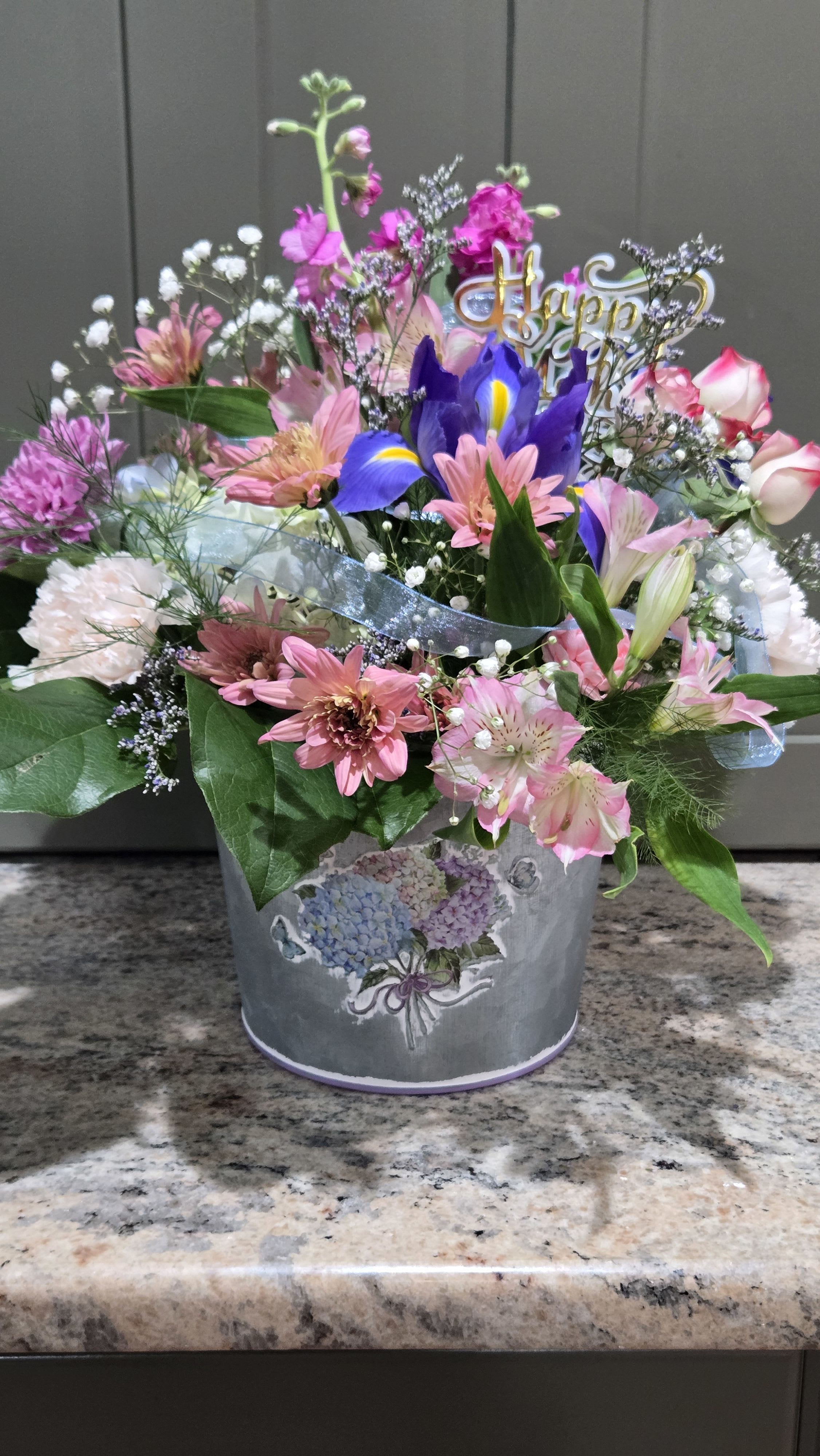  Mother's Blooms  - Keepsake Tin pot with hydrangea. The flower selection complimentary to the floral pattern, sheer stream of ribbon, with Caspia, Gyp accents. Happy Mothers Day pick finishes off the stunning Gift for Mother's Day week delivery!  Limited inventory available for holiday week and thereafter. DELUXE or Premium are not available for upgrades.
