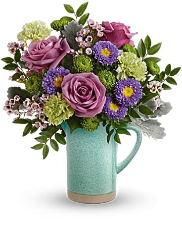 Purple roses and mixed blooms arranged in a turquoise pitcher vase