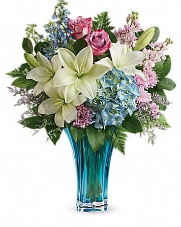 Bouquet of white lilies, pink roses, and blue hydrangeas in a blue glass vase