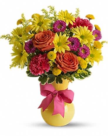 Colorful bouquet of roses, daisies, and carnations in a yellow vase with a pink ribbon.