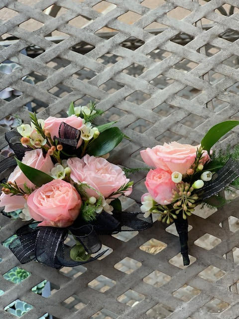Two small pink rose boutonnieres with black ribbon accents