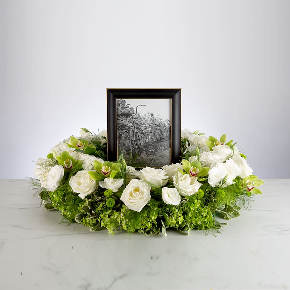 Round wreath of white roses and green orchids surrounding a framed black-and-white photo