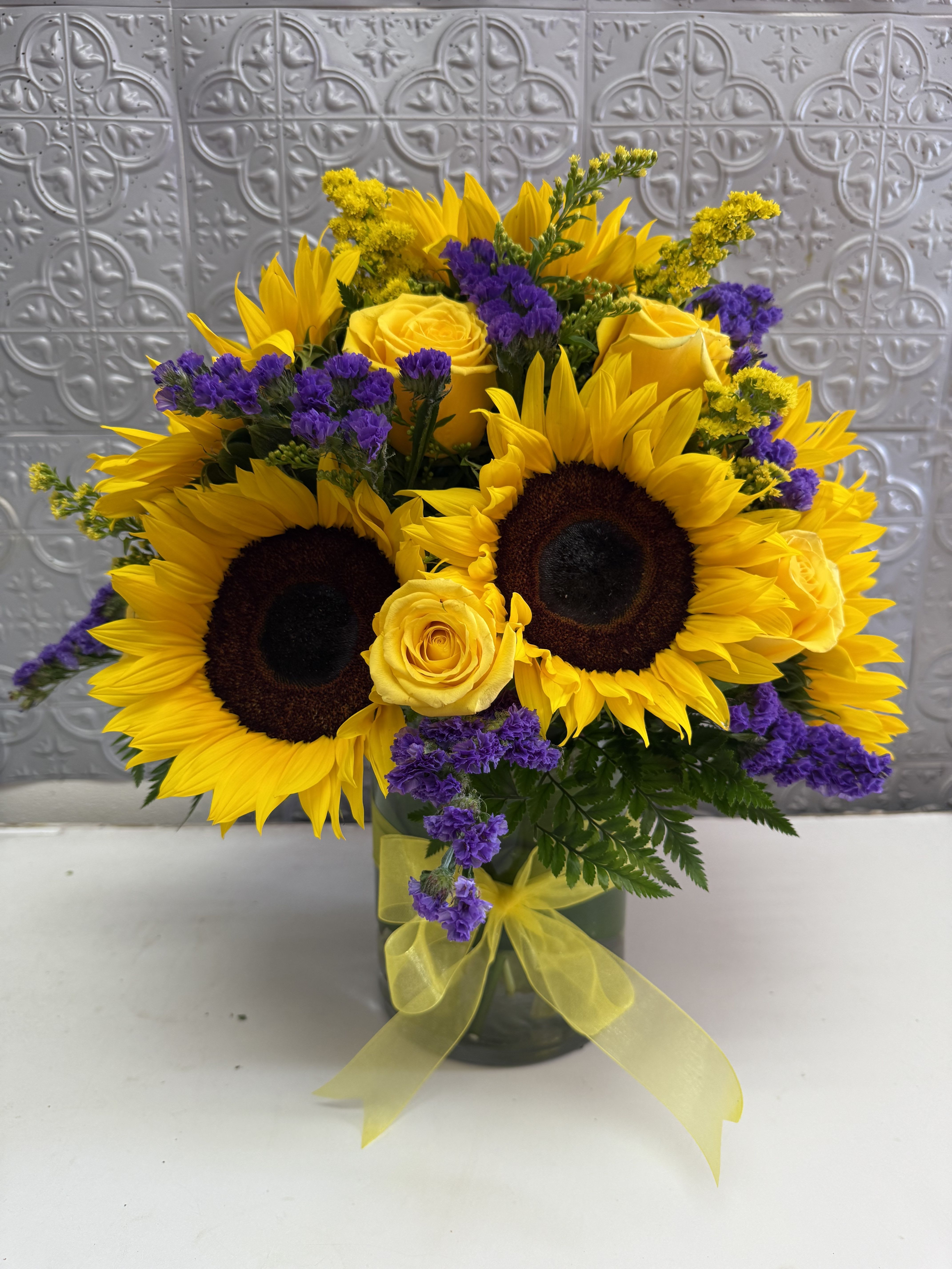 Sunflower and yellow rose bouquet in a glass vase with purple accents
