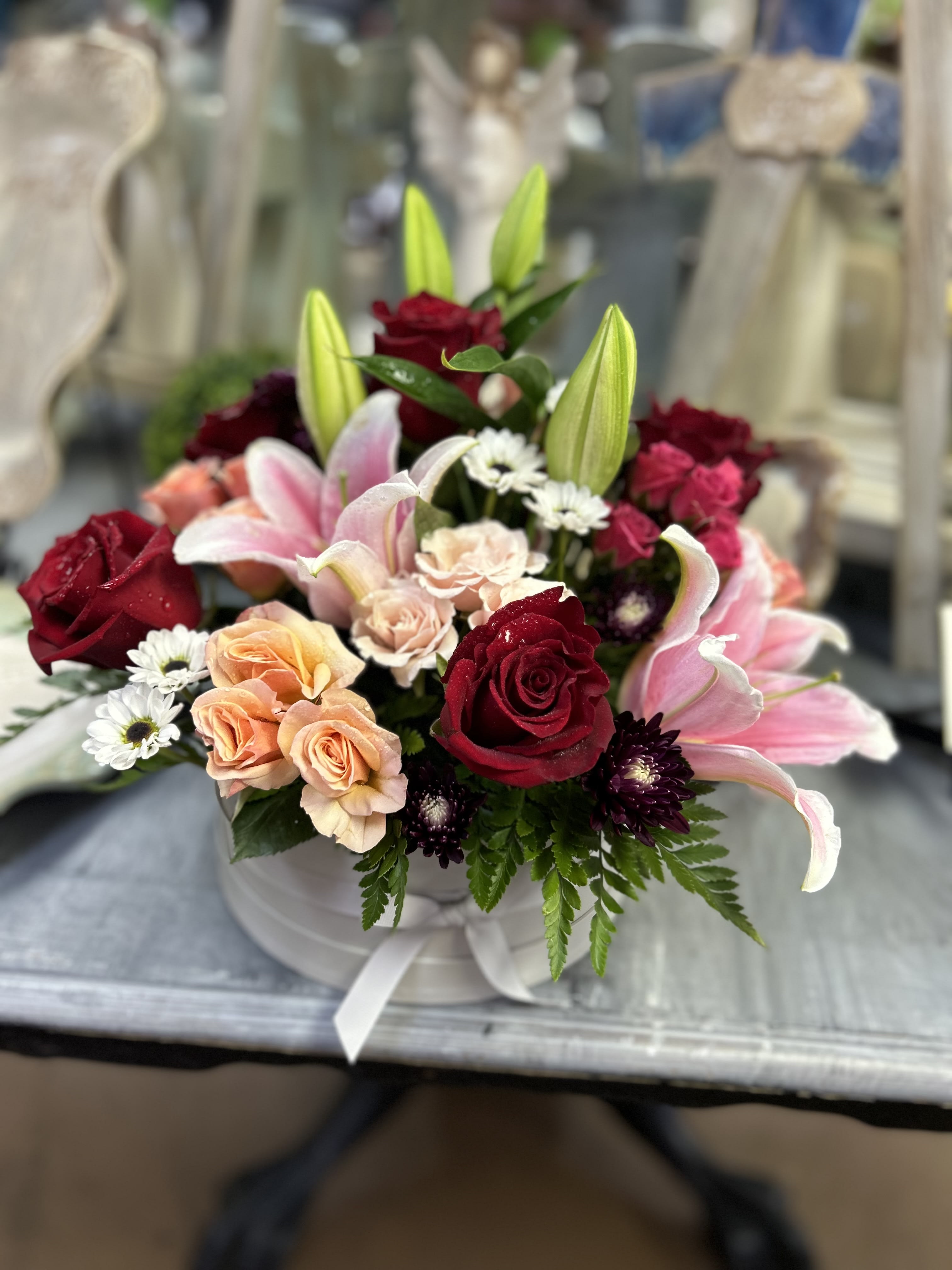 Mixed bouquet of red roses, pink lilies, and peach spray roses in a white hatbox