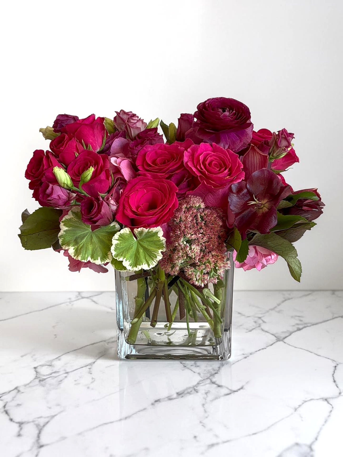 Vivid Dream - A lush cluster of vivid pink roses and dramatic cymbidium orchids creates an immediate romantic impression-perfect as a love and romance arrangement or a Valentine's Day gift that feels both luxurious and intimate. The low, full composition sits in a clear square glass vase so the recipient sees the layered petals and rich color from every angle.  PLEASE NOTE: Substitutions will be made depending on availability. We shop fresh and we value quality over anything else. We will try our very best to maintain the overall look and presentation of this design.