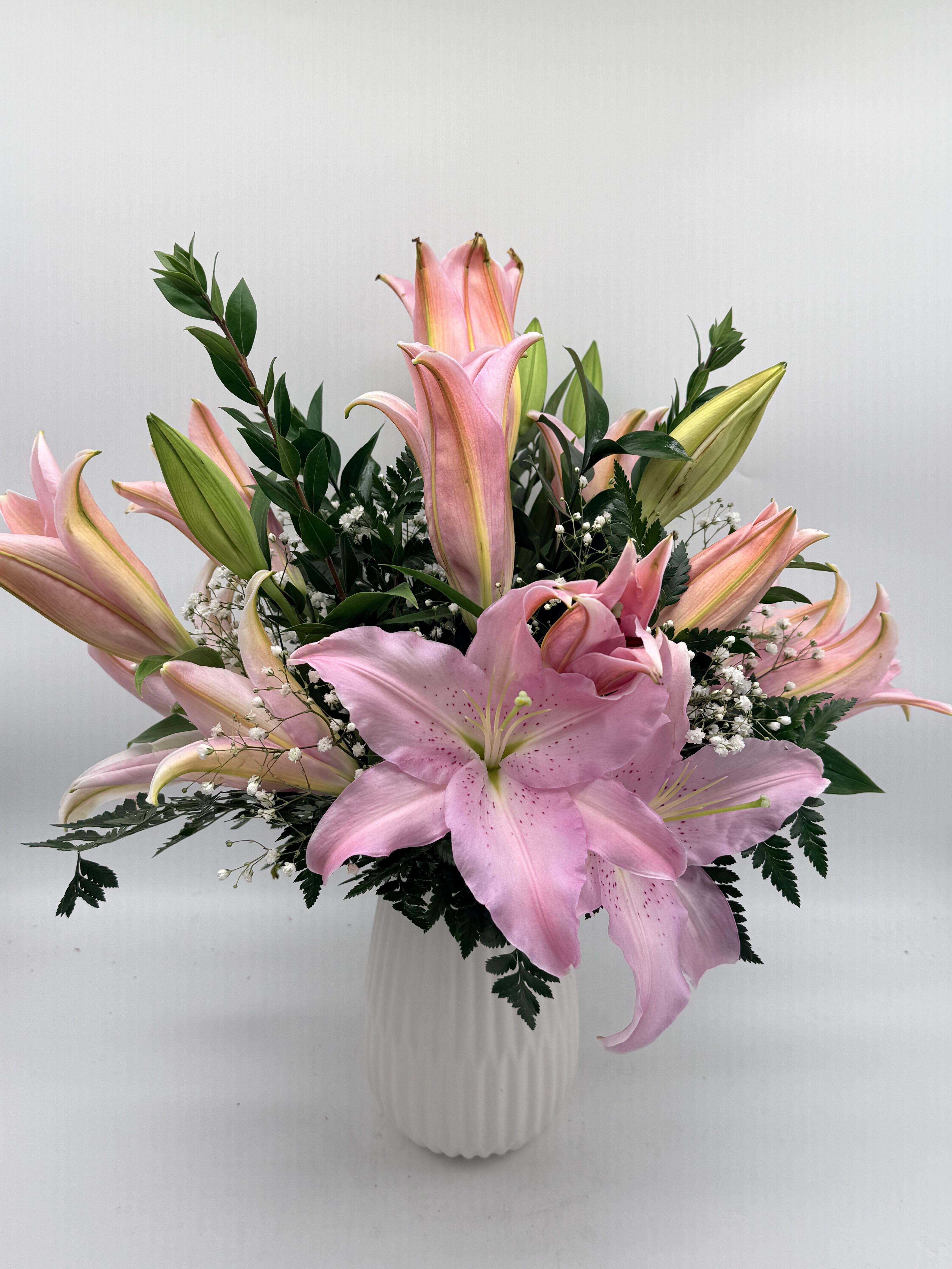 Pink lilies arranged in a white vase with greenery
