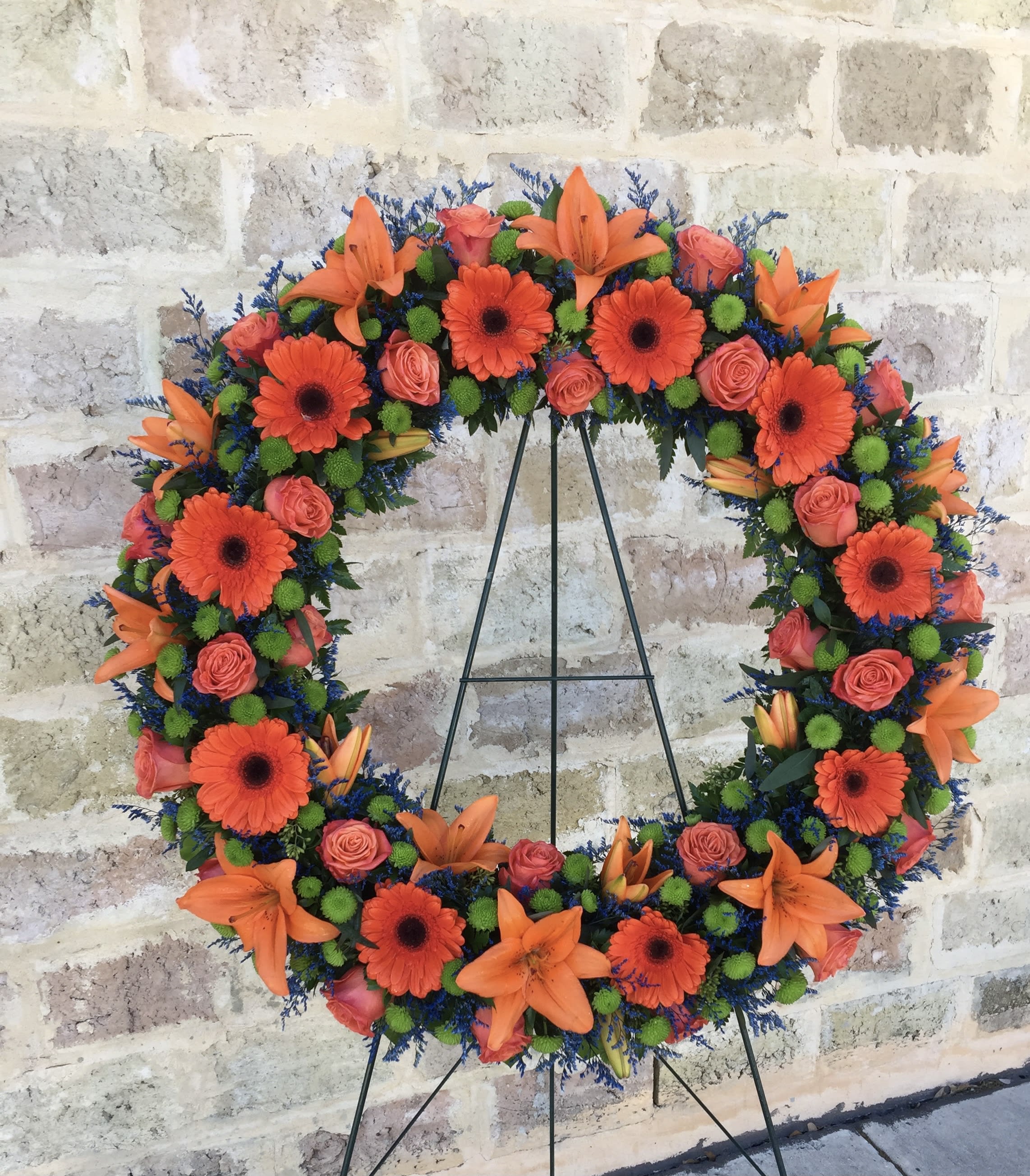Circular floral wreath with orange lilies, gerbera daisies, and pink roses on a stand