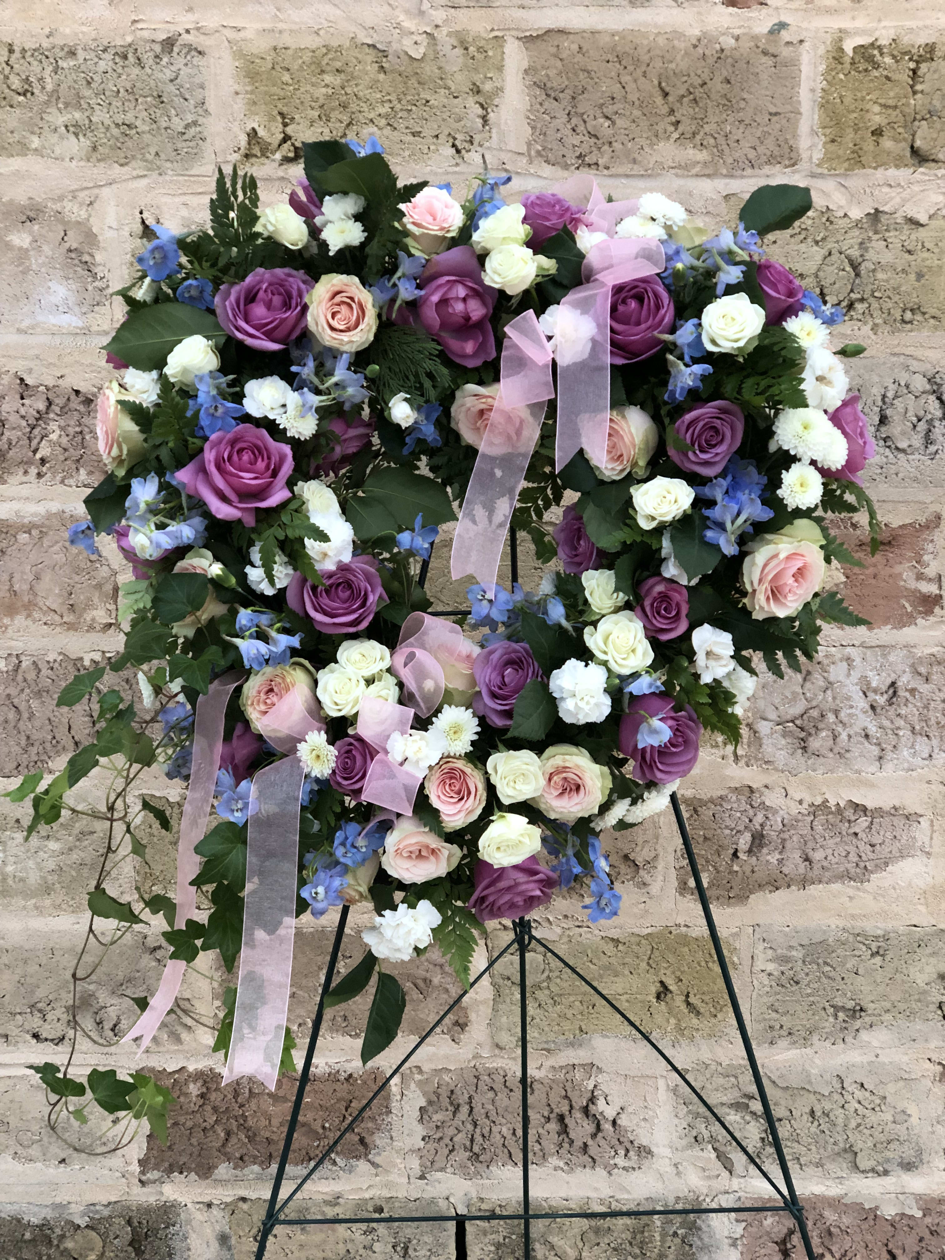 Heart-shaped floral wreath with purple, pink, and white roses on a stand