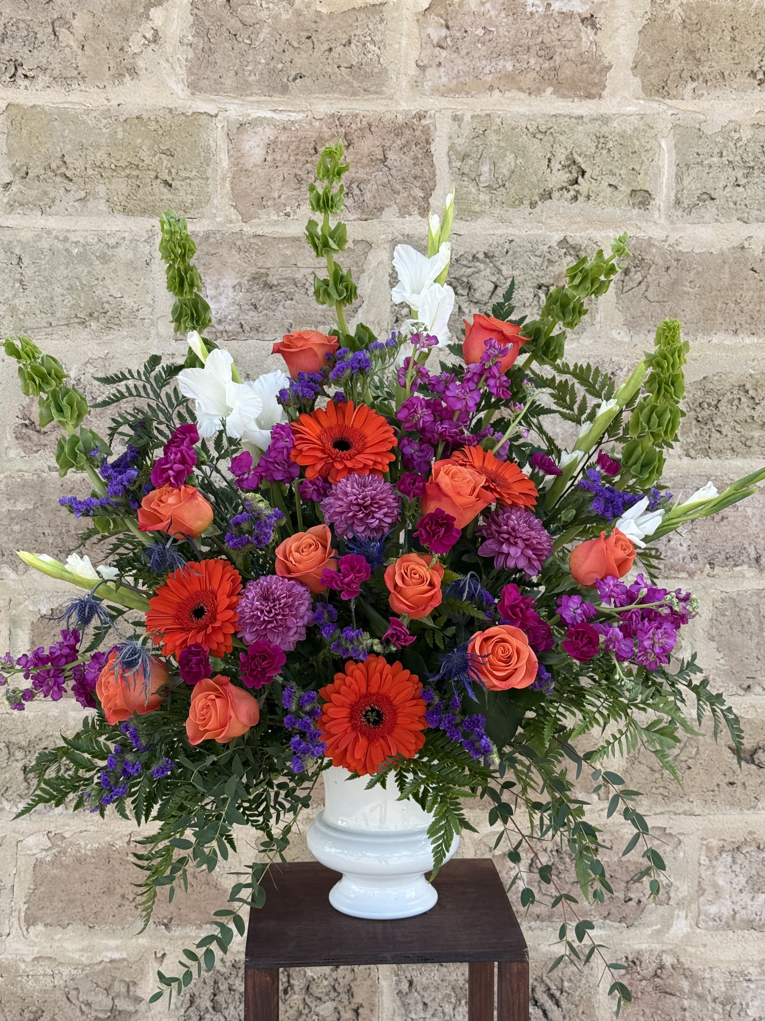 Bright mixed flower arrangement in a white vase with orange and purple blooms