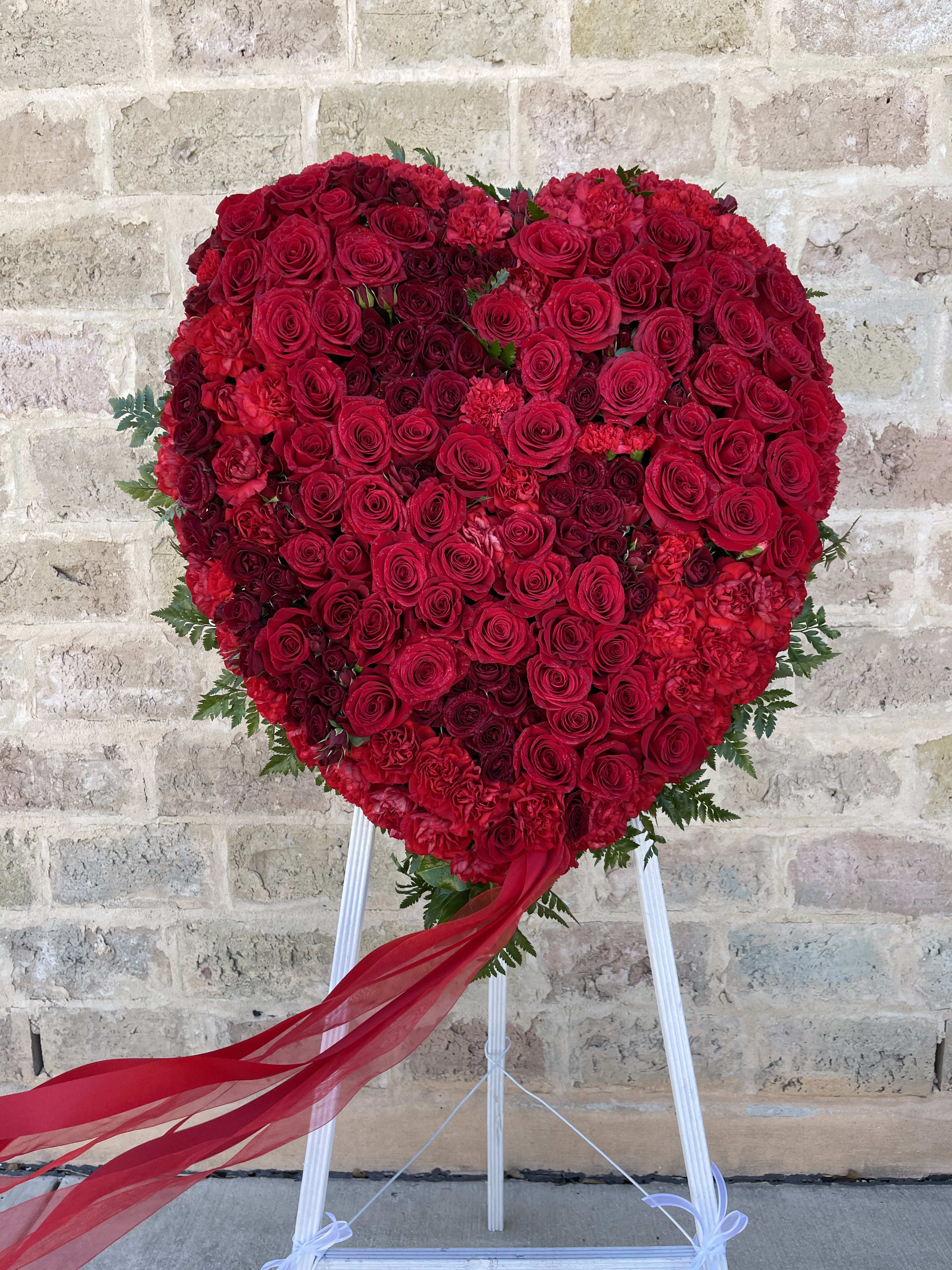 Heart-shaped red rose arrangement on a stand with a flowing ribbon