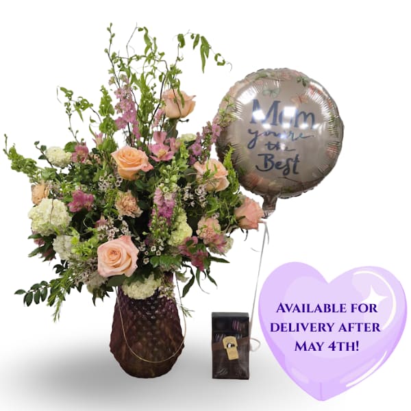 Forever Blooms Bundle - Peach roses and pink alstroemeria take center stage in this Mother's Day flower arrangement, the Forever Blooms Bundle crafted to make the person you're thinking of feel celebrated and deeply appreciated. Designed as a gift-ready bouquet for Mother's Day or a special birthday, its soft palette of pink, peach, white, and green reads warm and affectionate-exactly the message a mother, grandmother, or mentor should receive.  This garden-style design layers peach roses, pale carnations, pink alstroemeria, viburnum, tall pink larkspur, delicate wax flower accents, and loose branching greenery for an airy, full silhouette. The blooms sit in a tall textured glass or decorative dark vase (available as shown or in a giant pink vase on request), with softer flowers clustered at the base and taller stems rising above for elegant height and movement. A round metallic/foil balloon that reads "Mom you're the Best" and a small chocolate box are included, turning the arrangement into a complete gift set.  Perfect for Mother's Day, a milestone birthday, or to say "thank you" in a meaningful way, the Forever Blooms Bundle arrives ready to present-no fuss, just a joyful, affectionate statement. 