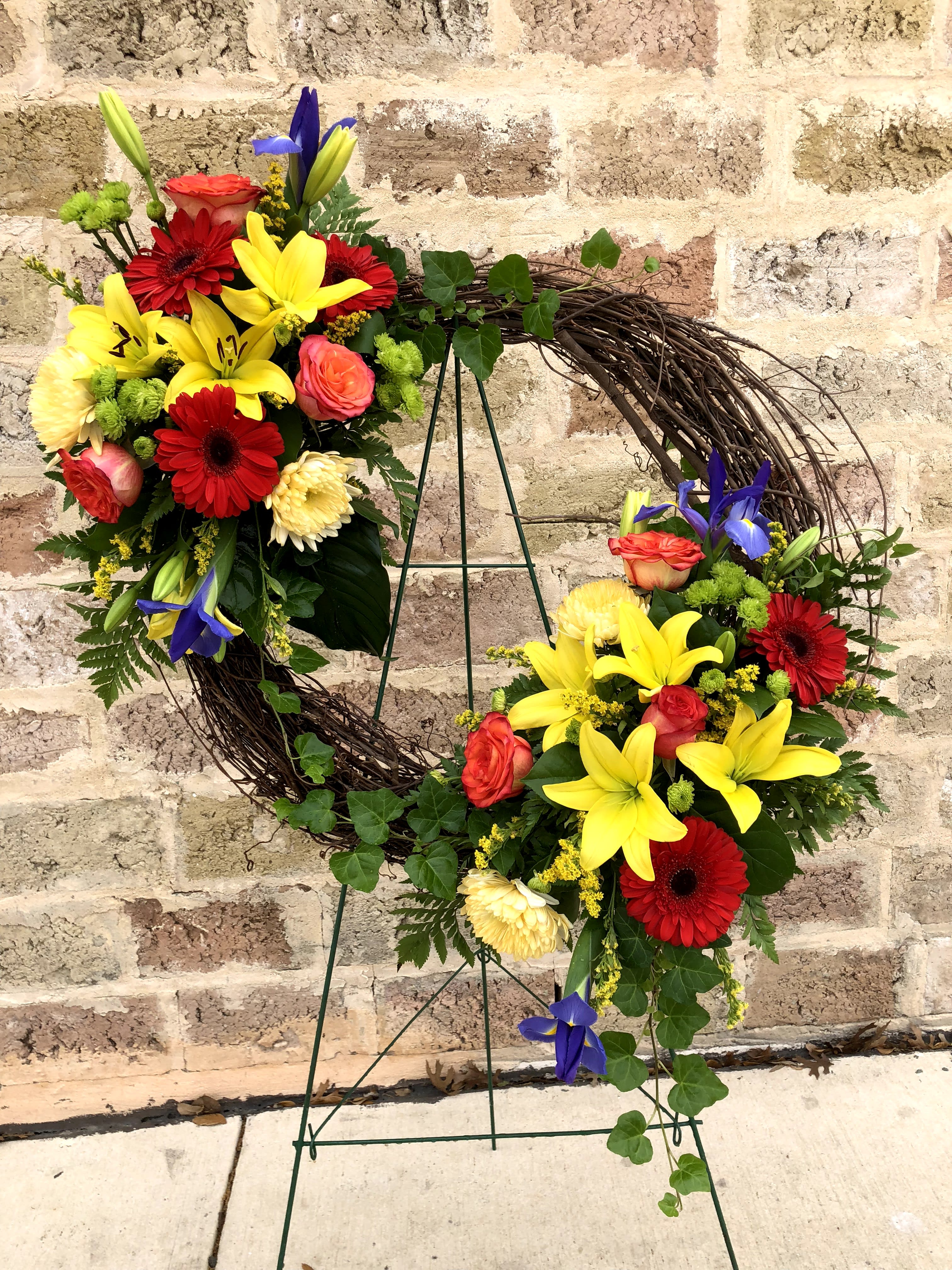Circular floral wreath with red, yellow, and pink blooms on a metal stand