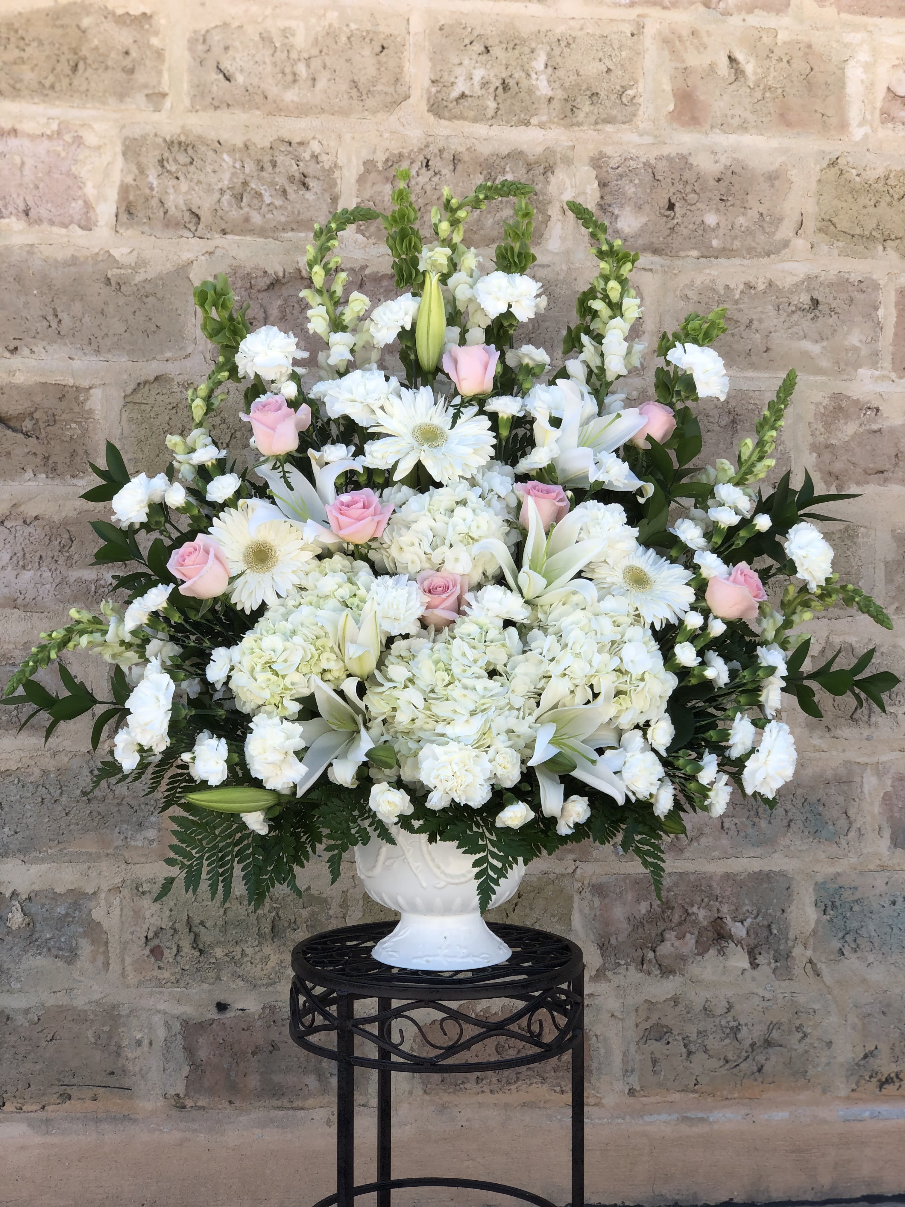 White floral arrangement with pink roses in a white urn vase