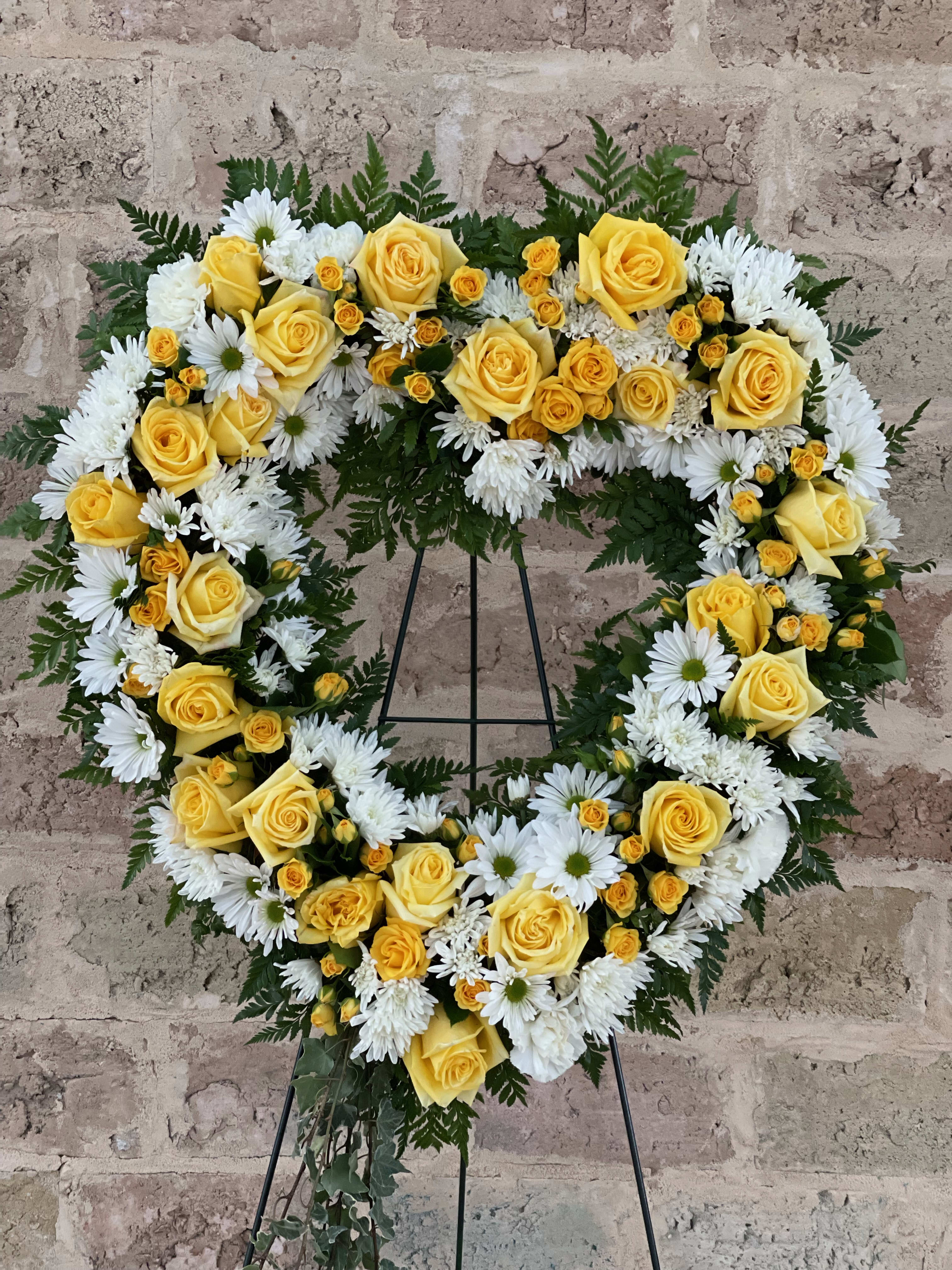 Heart-shaped floral wreath with yellow roses and white daisies on a stand