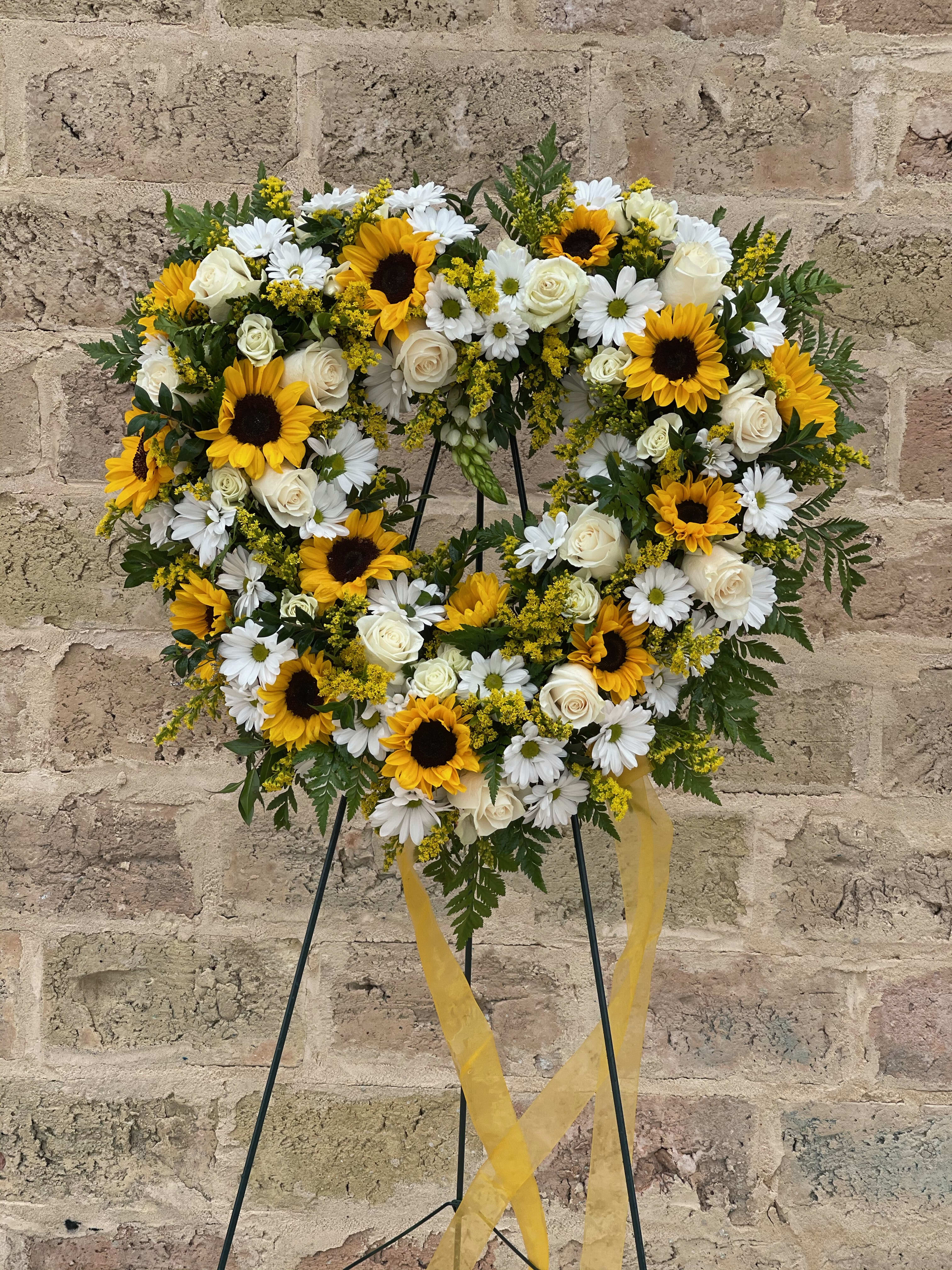 Heart-shaped floral wreath with sunflowers, white roses, and daisies on a stand