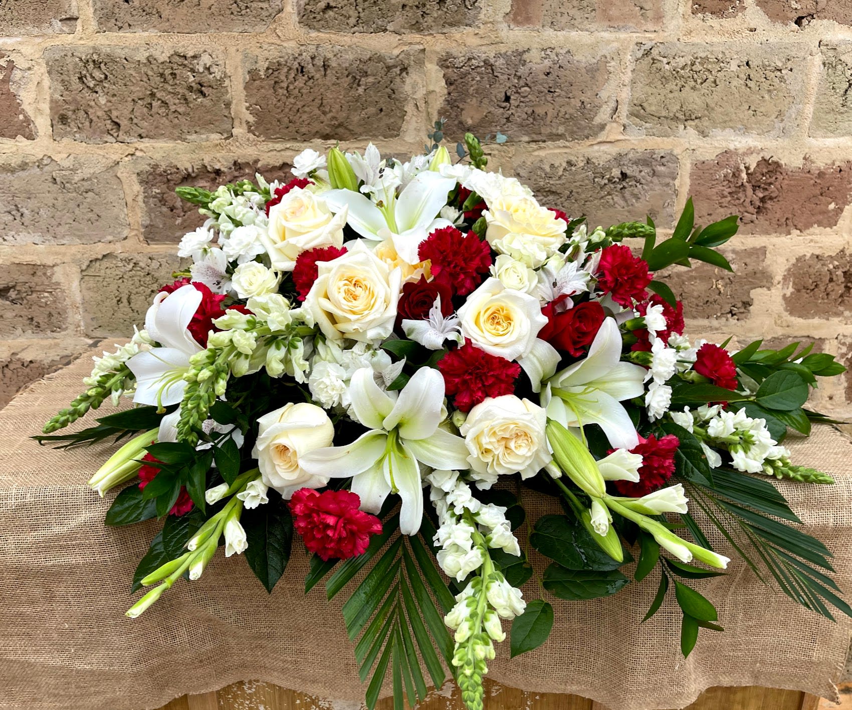 Red and white funeral spray with lilies, roses, carnations, and snapdragons in an elongated design