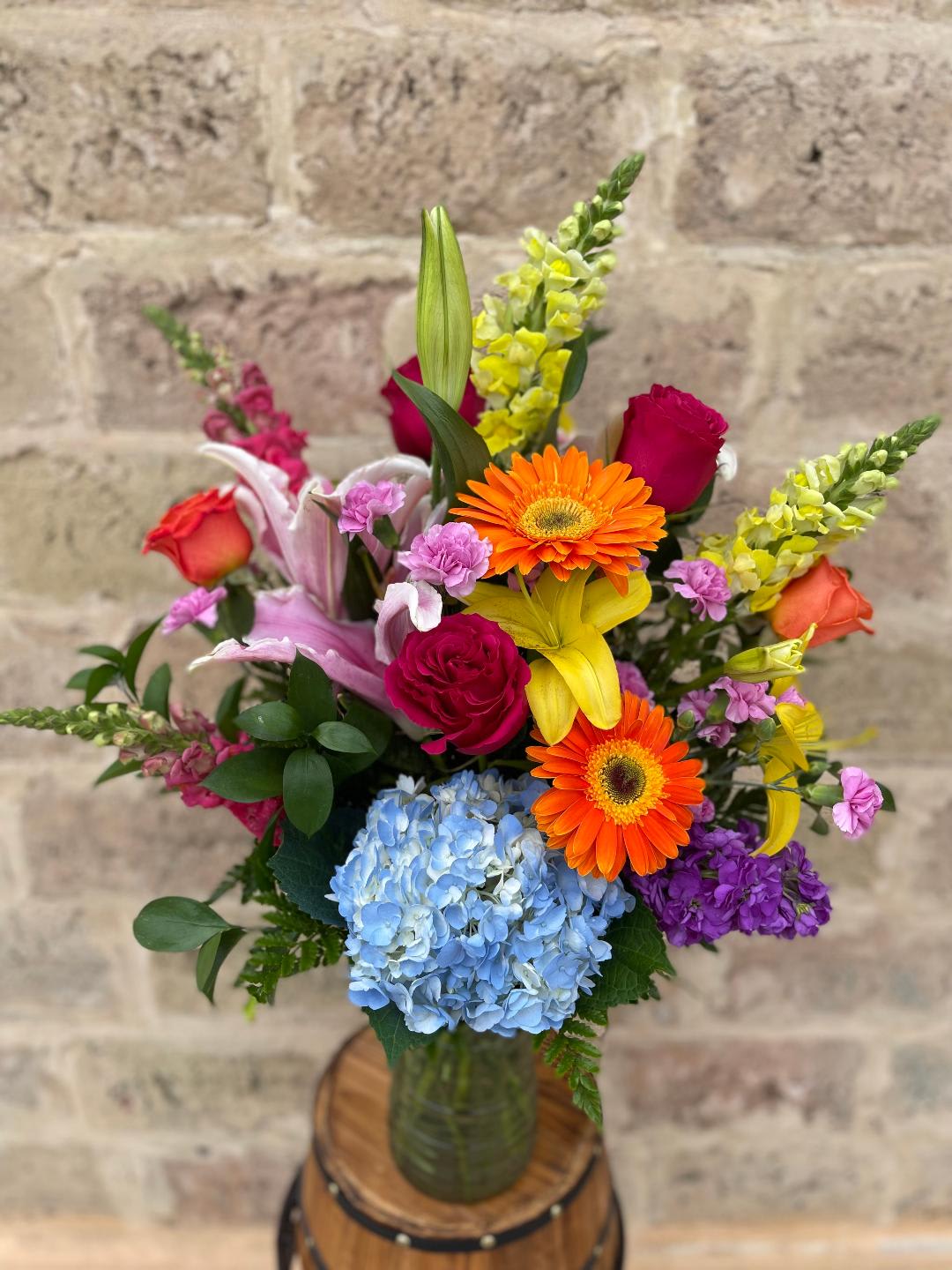 Colorful mixed bouquet in a glass vase with roses, lilies, gerbera daisies, and hydrangea