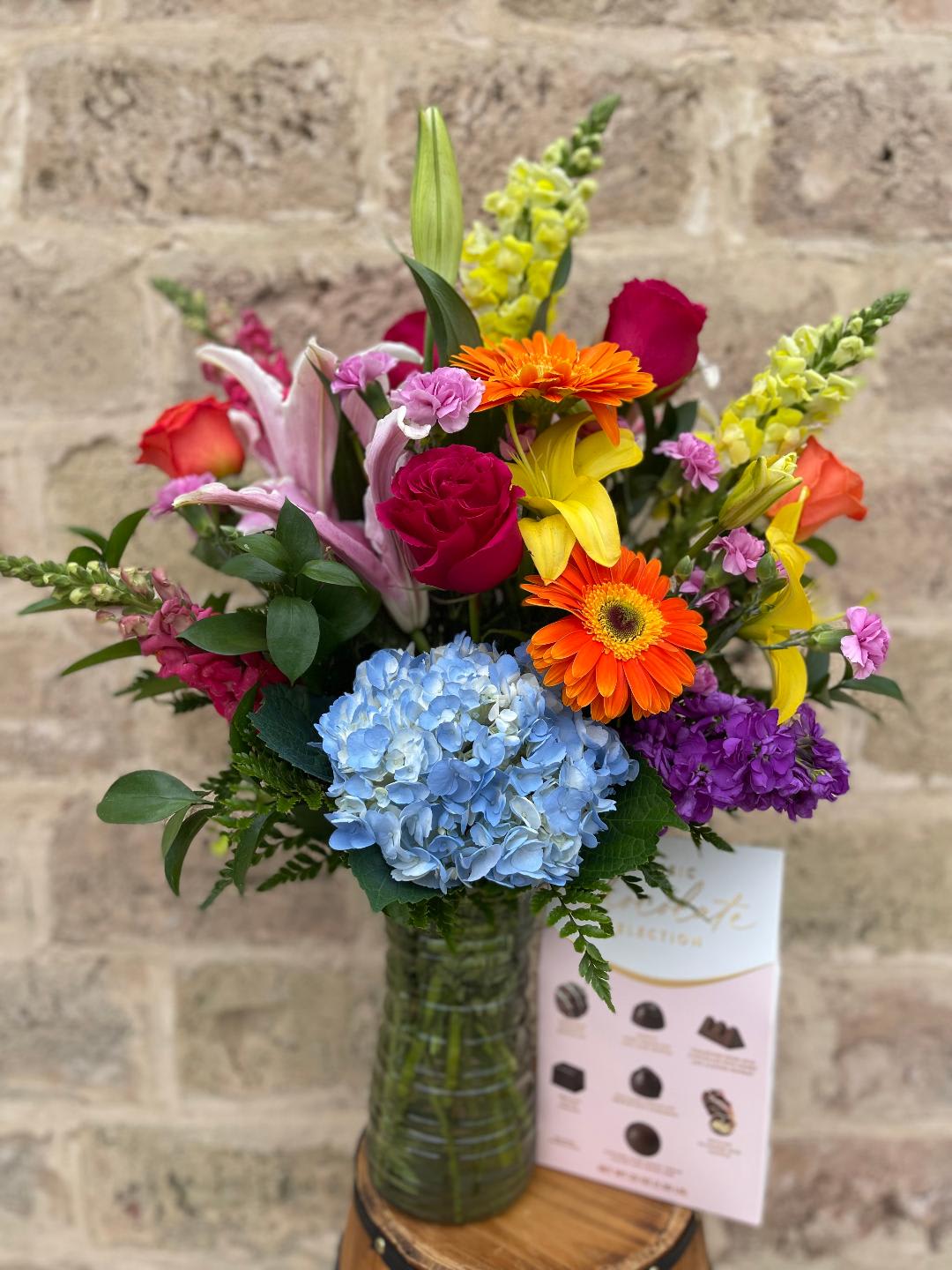 Colorful mixed bouquet in a glass vase with roses, lilies, gerbera daisies, and hydrangea