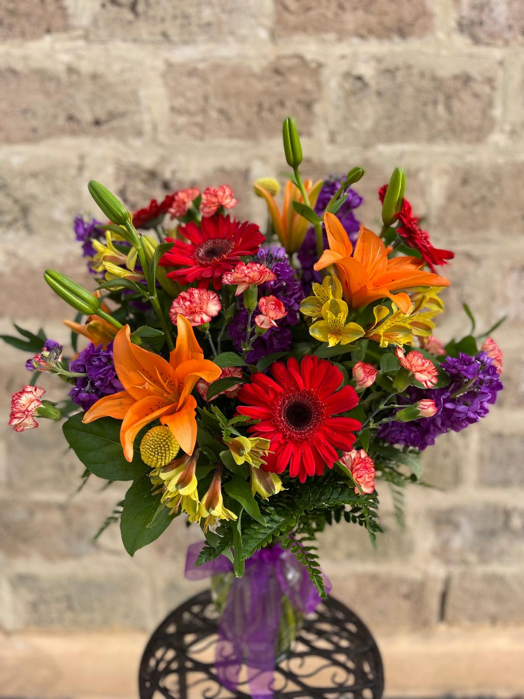 Colorful bouquet with orange lilies, red gerbera daisies, and purple flowers in a vase