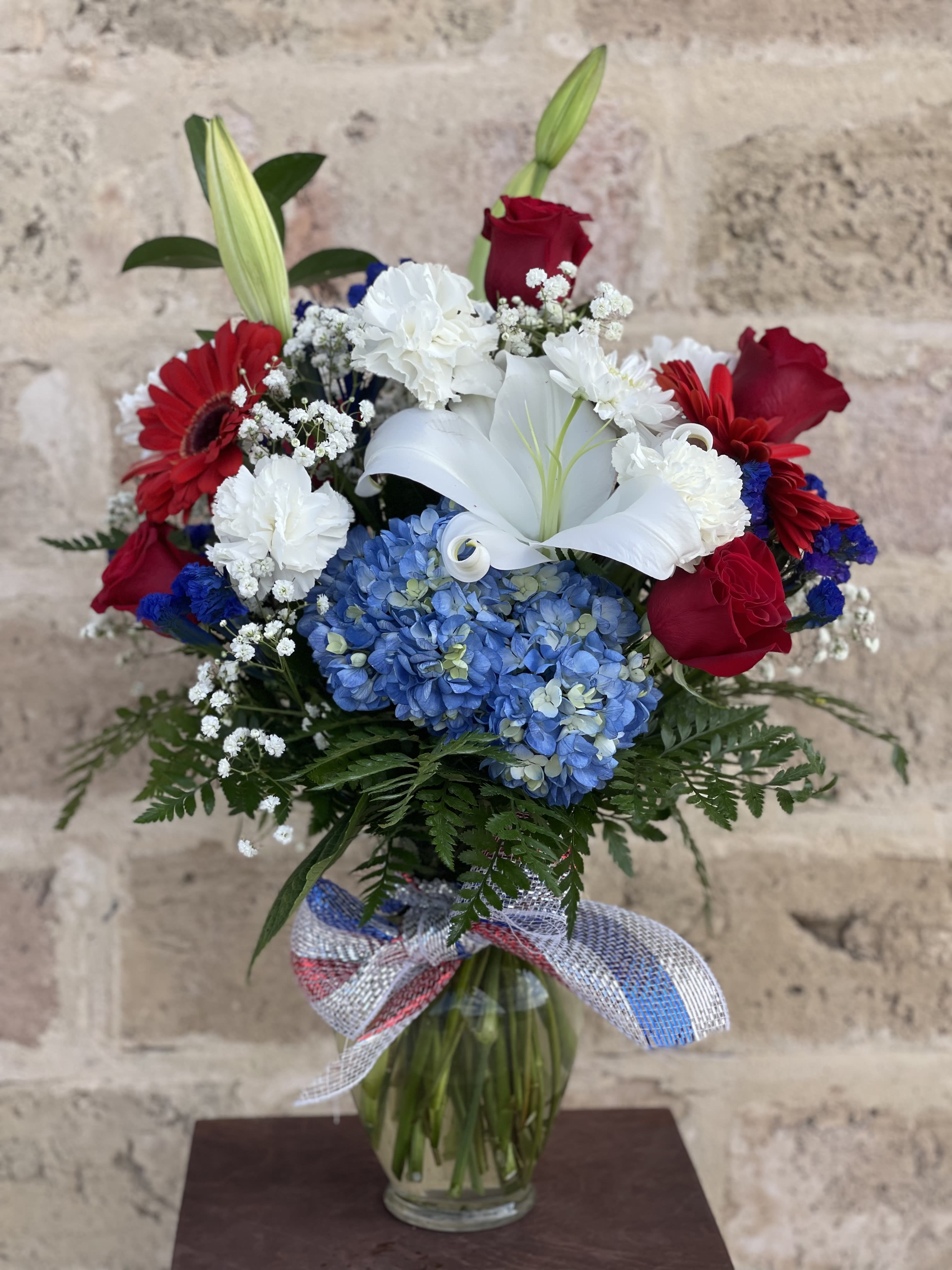 Bouquet of red roses, white lilies, and blue hydrangeas in a glass vase