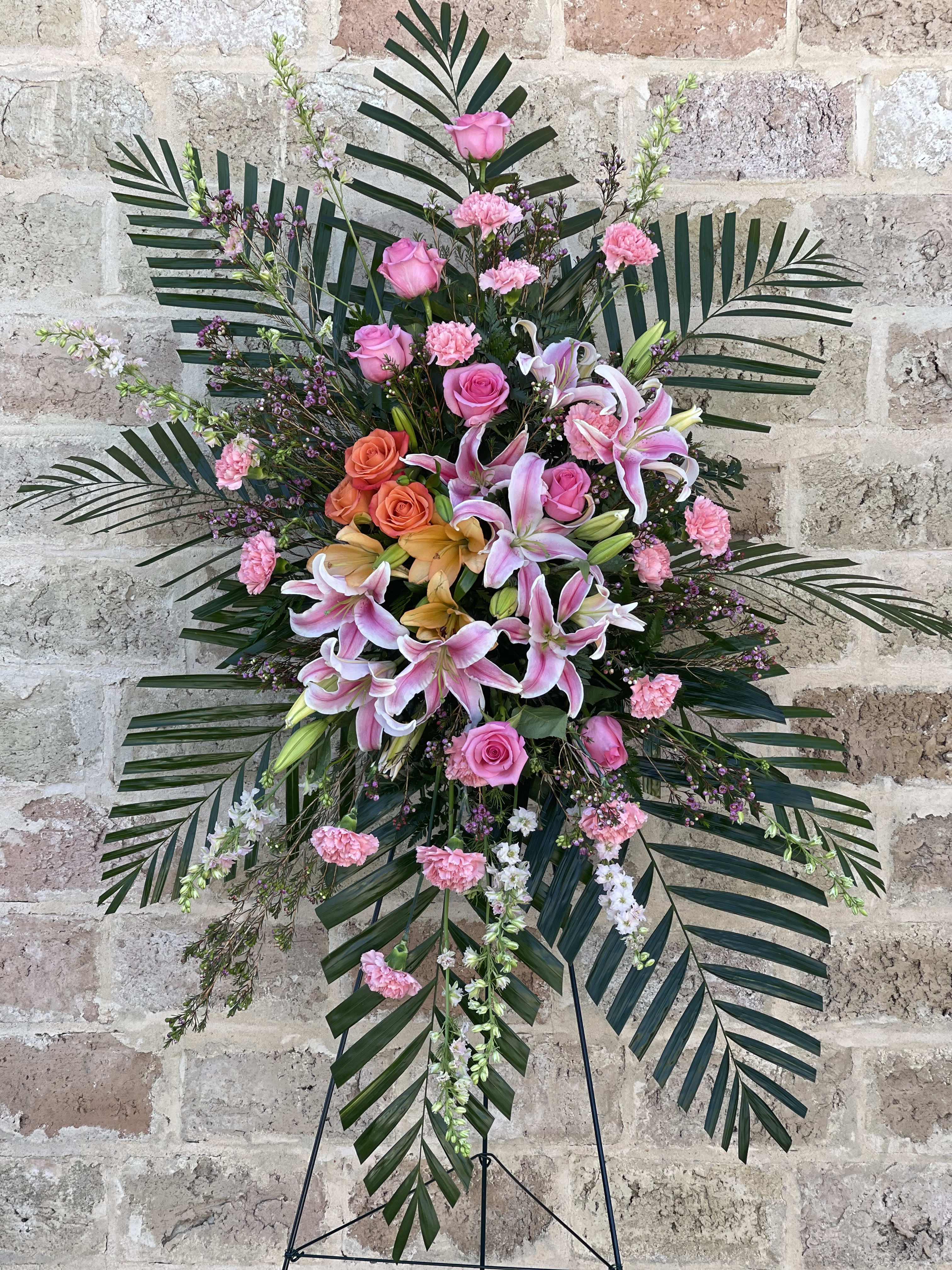 Spirit of Hope Standing Spray - Share the spirit of hope and faith with a generous standing spray of pink and orange blossoms – including lilies, roses and carnations – against a backdrop of fresh palm fronds. A lovely way to express your sympathies.