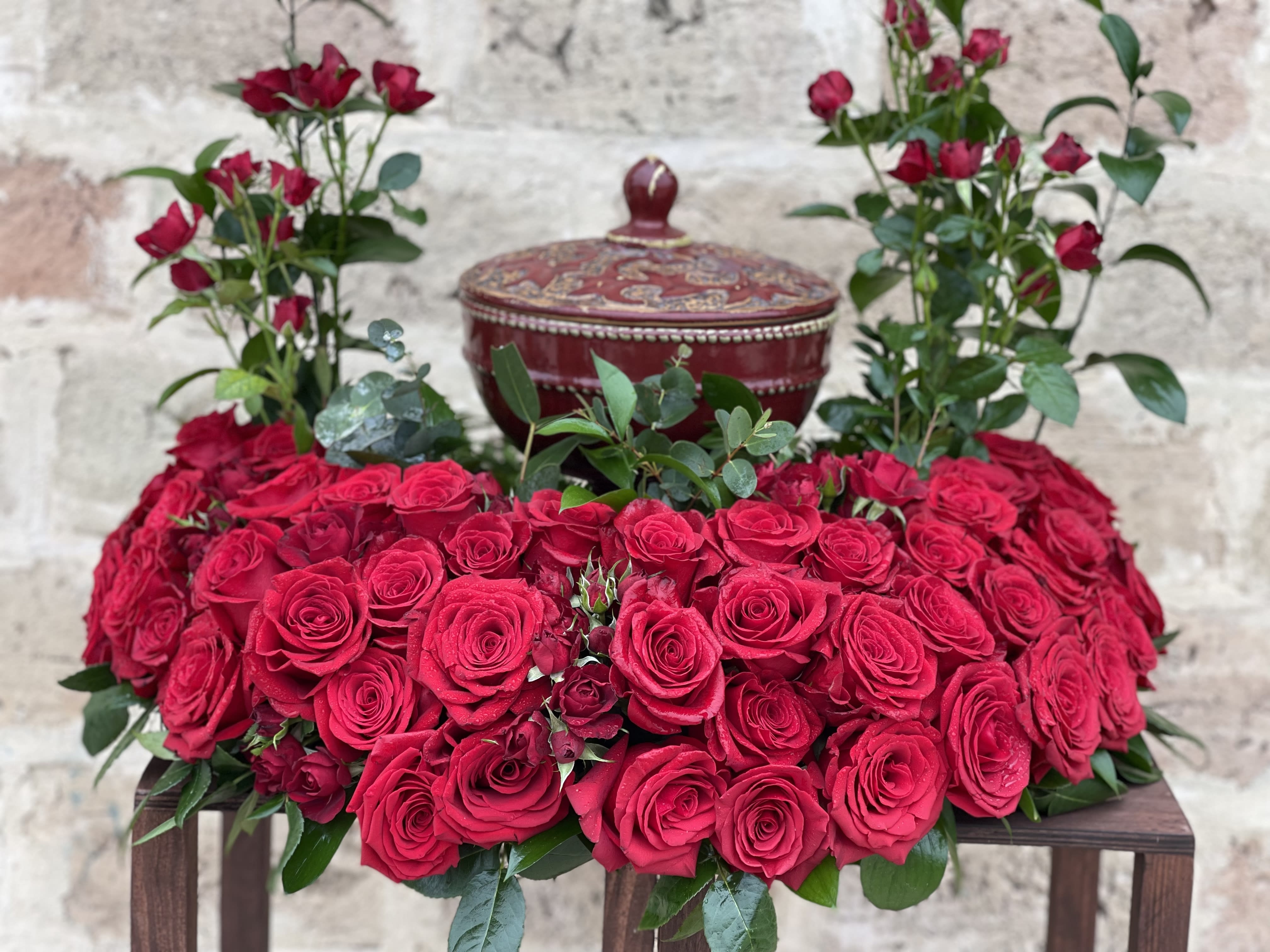 Heart-shaped arrangement of red roses with a decorative lidded box behind it