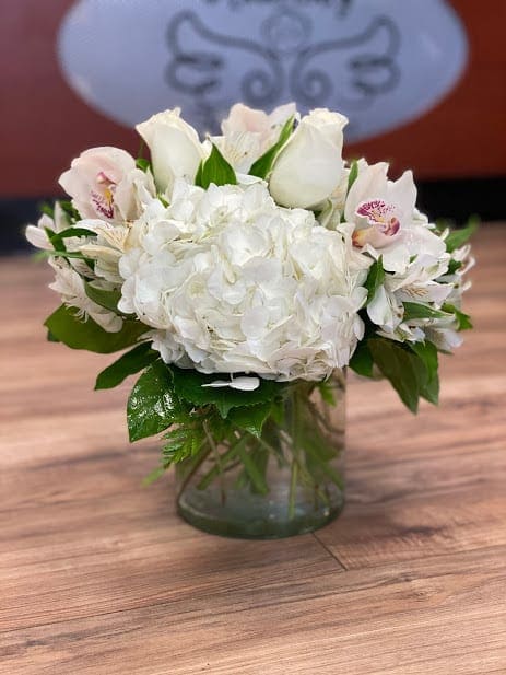 White hydrangea and pale pink orchid arrangement in a glass vase