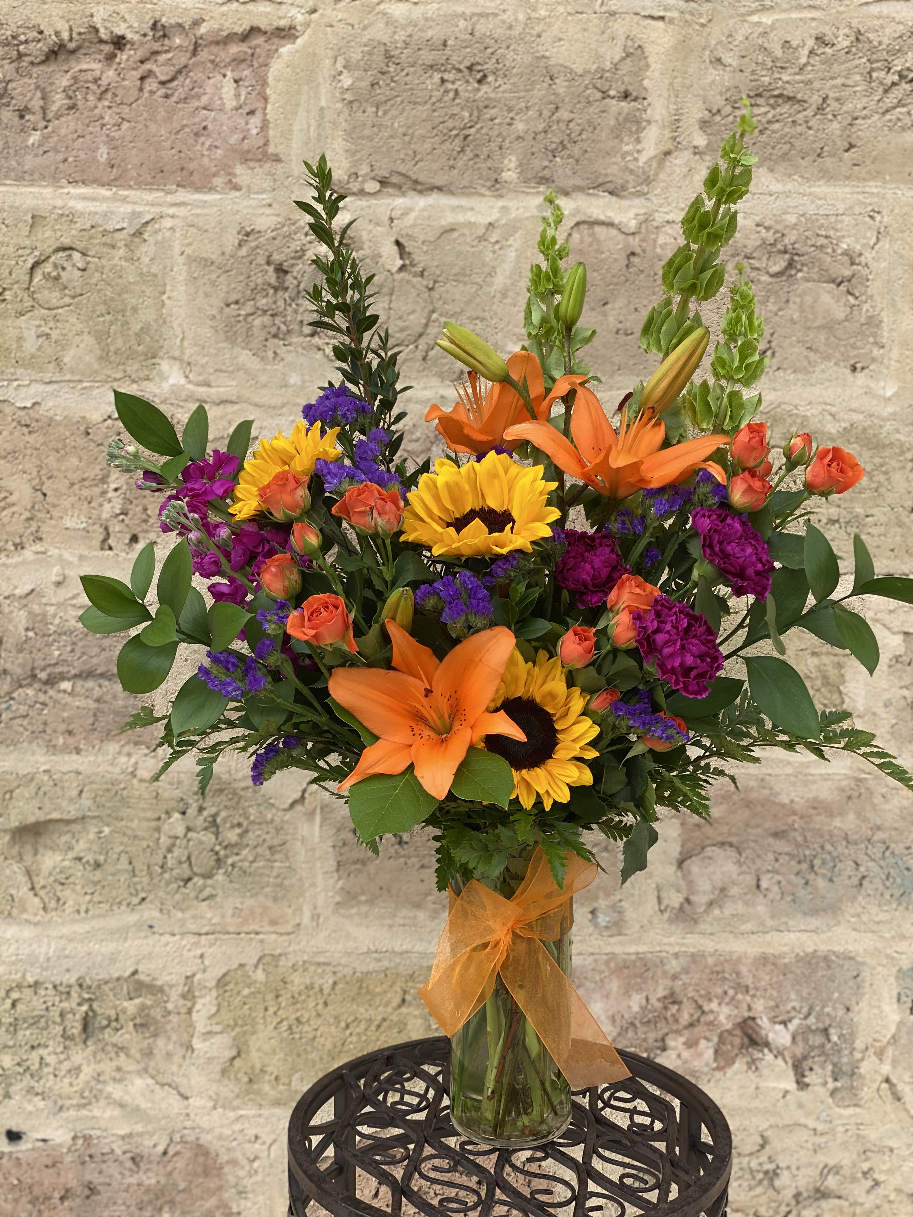 Bouquet of orange lilies, sunflowers, and purple flowers in a glass vase