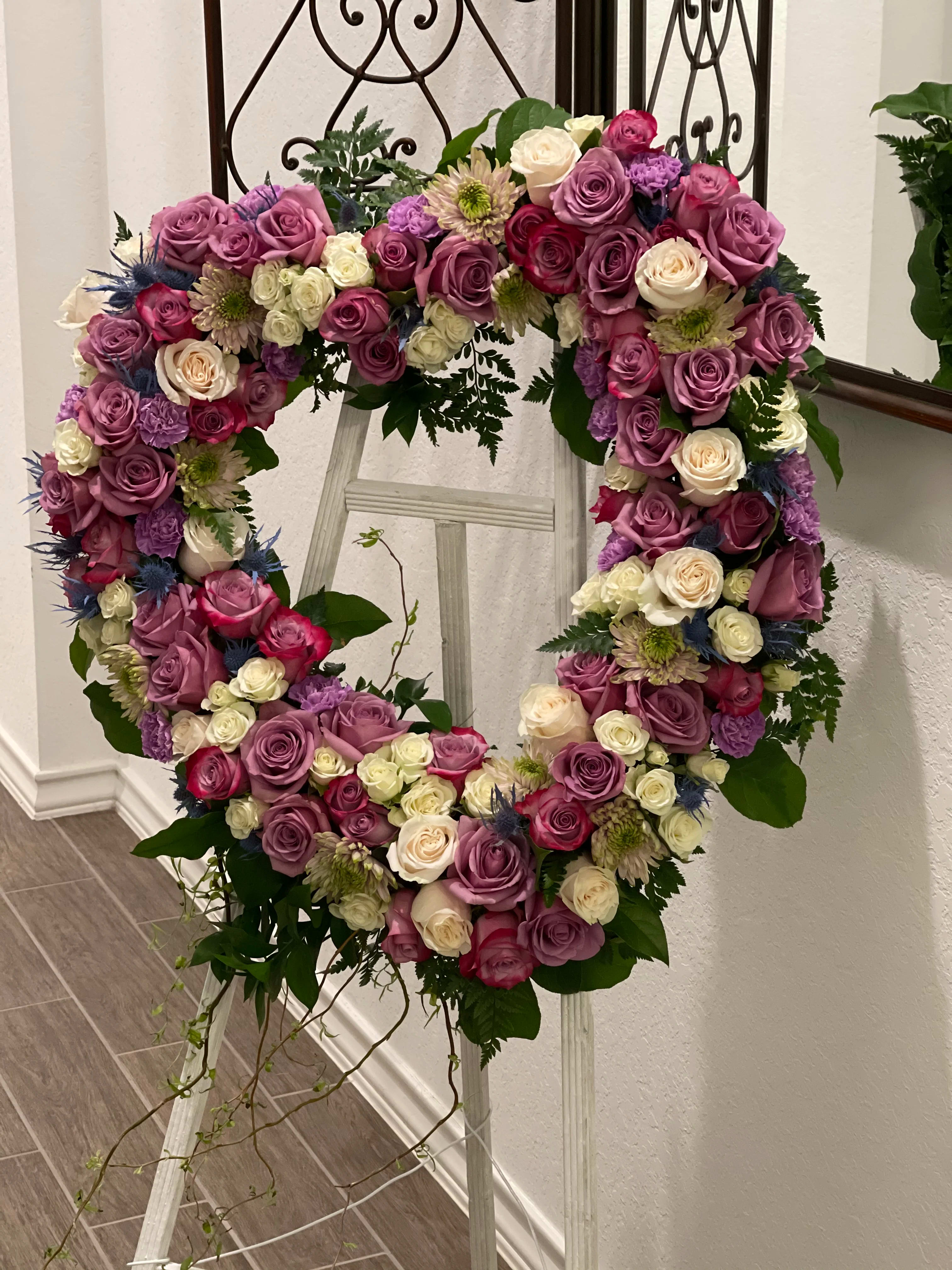 Heart-shaped floral wreath of pink, purple, and white roses on a stand