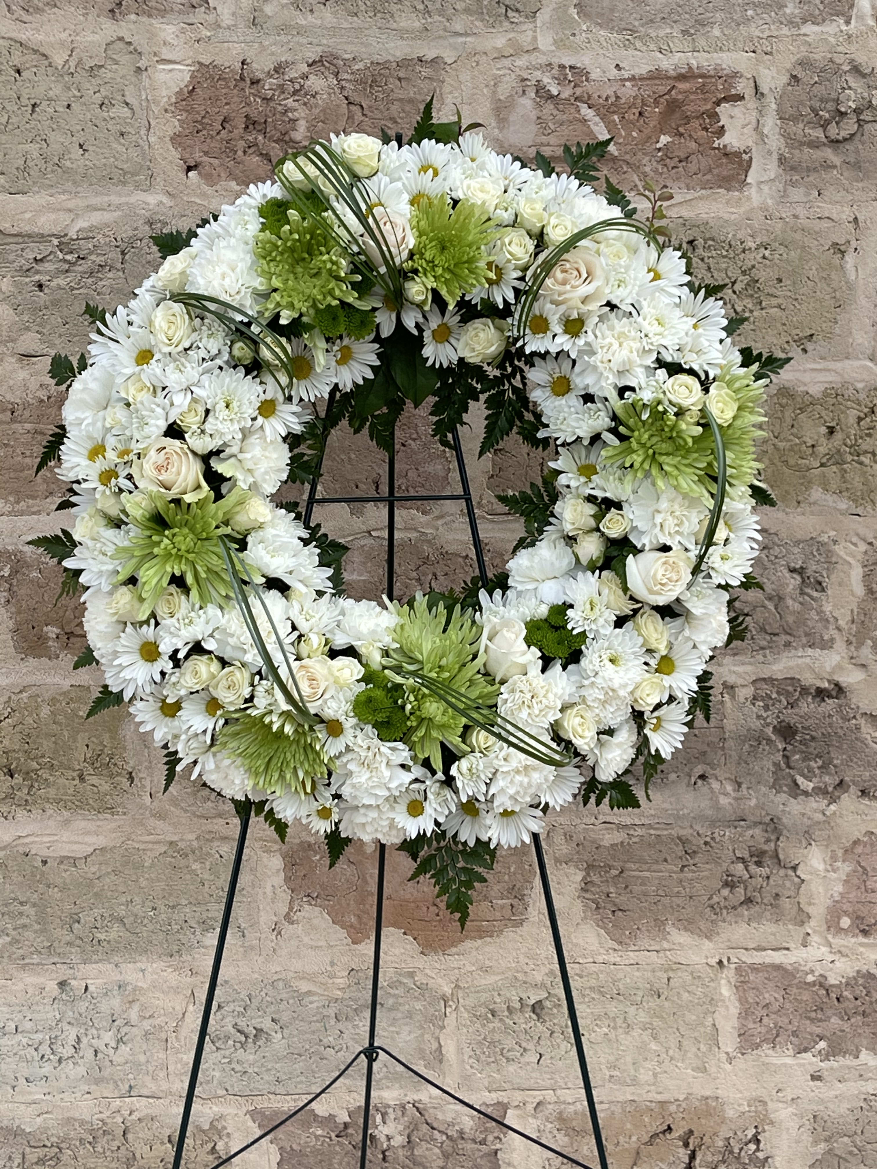 White and green floral wreath on a black stand