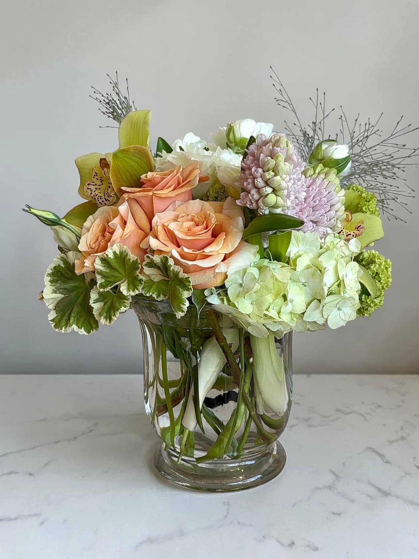 Peachy Punch  - Peachy peach roses and pale green hydrangeas set a soft, romantic tone in this mixed bouquet-perfect as a Mother's Day bouquet, birthday surprise, or just-because pick-me-up. The rounded, full composition is lifted by airy branching accents and soft pink clustered blooms that give height and delicate texture, so the person you're thinking of will feel genuinely celebrated the moment they see it. PLEASE NOTE: Substitutions will be made depending on availability. We shop fresh and we value quality over anything else. We will try our very best to maintain the overall look and presentation of this design. 