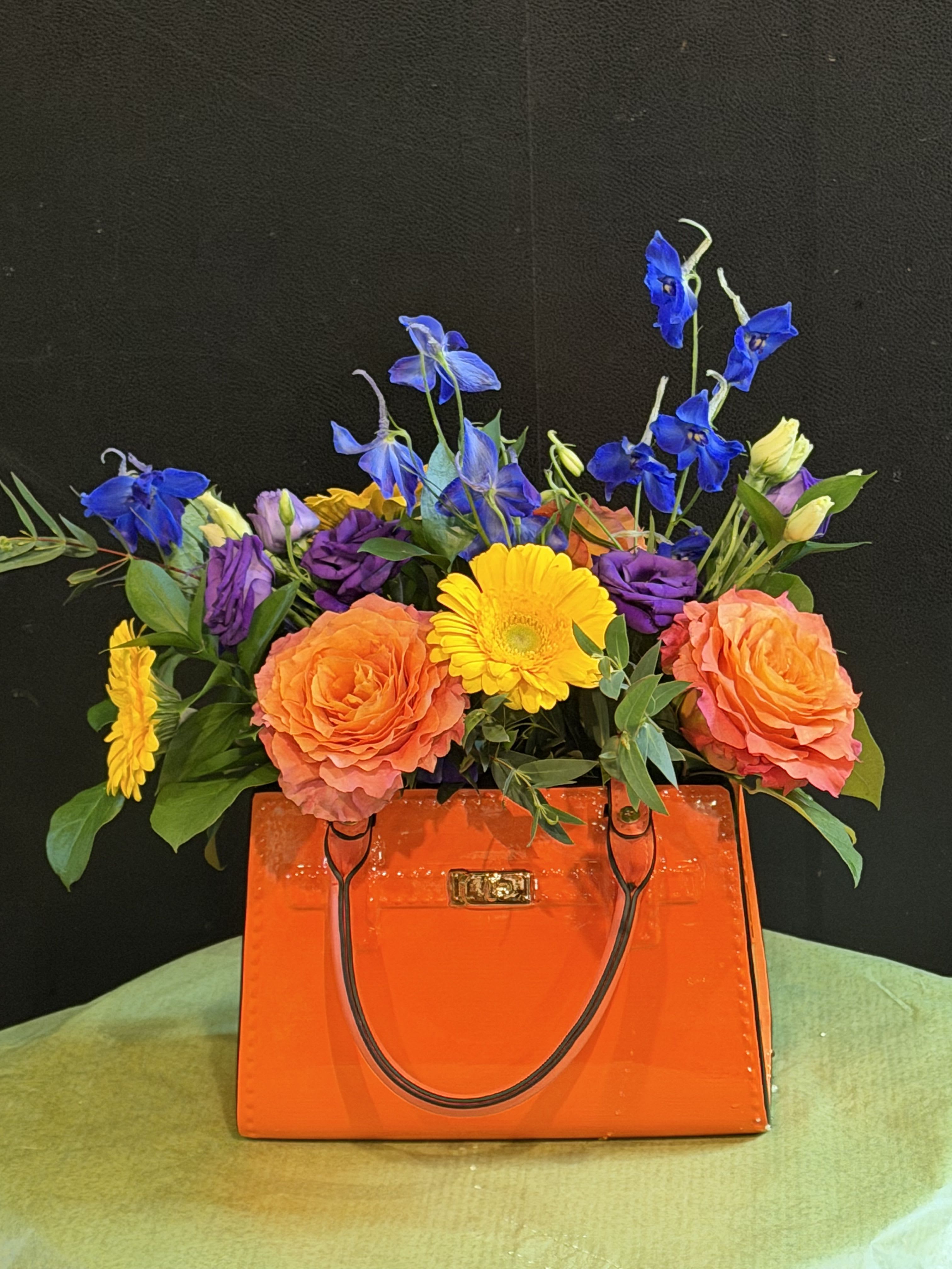 Vibrant Vogue - A bold, vibrant burst of color that makes a statement! Warm oranges and sunny yellows meet rich purples and blues in this show-stopping handbag arrangement. 