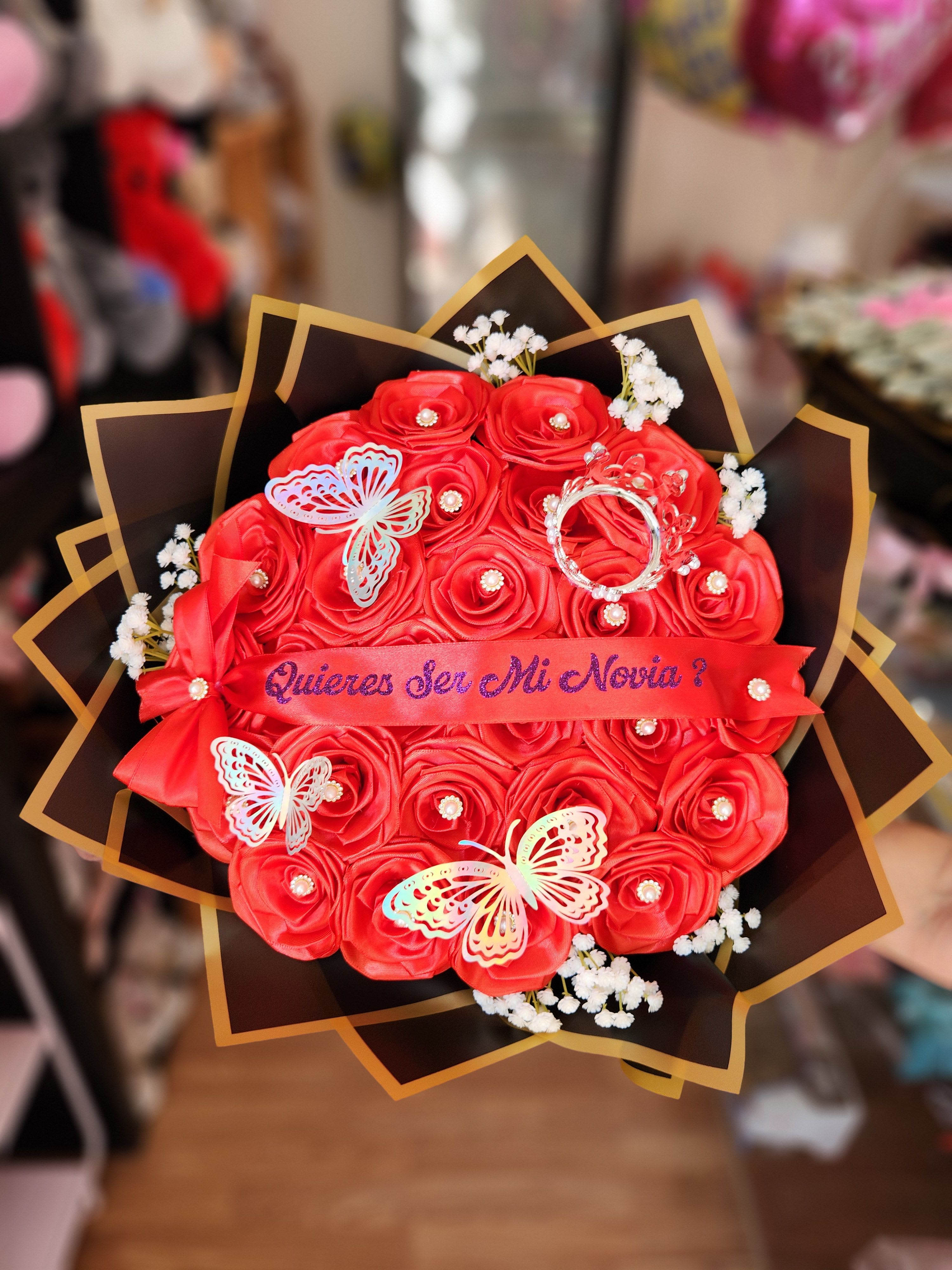 Red rose bouquet with butterflies and a ribbon reading "Quieres Ser Mi Novia?"