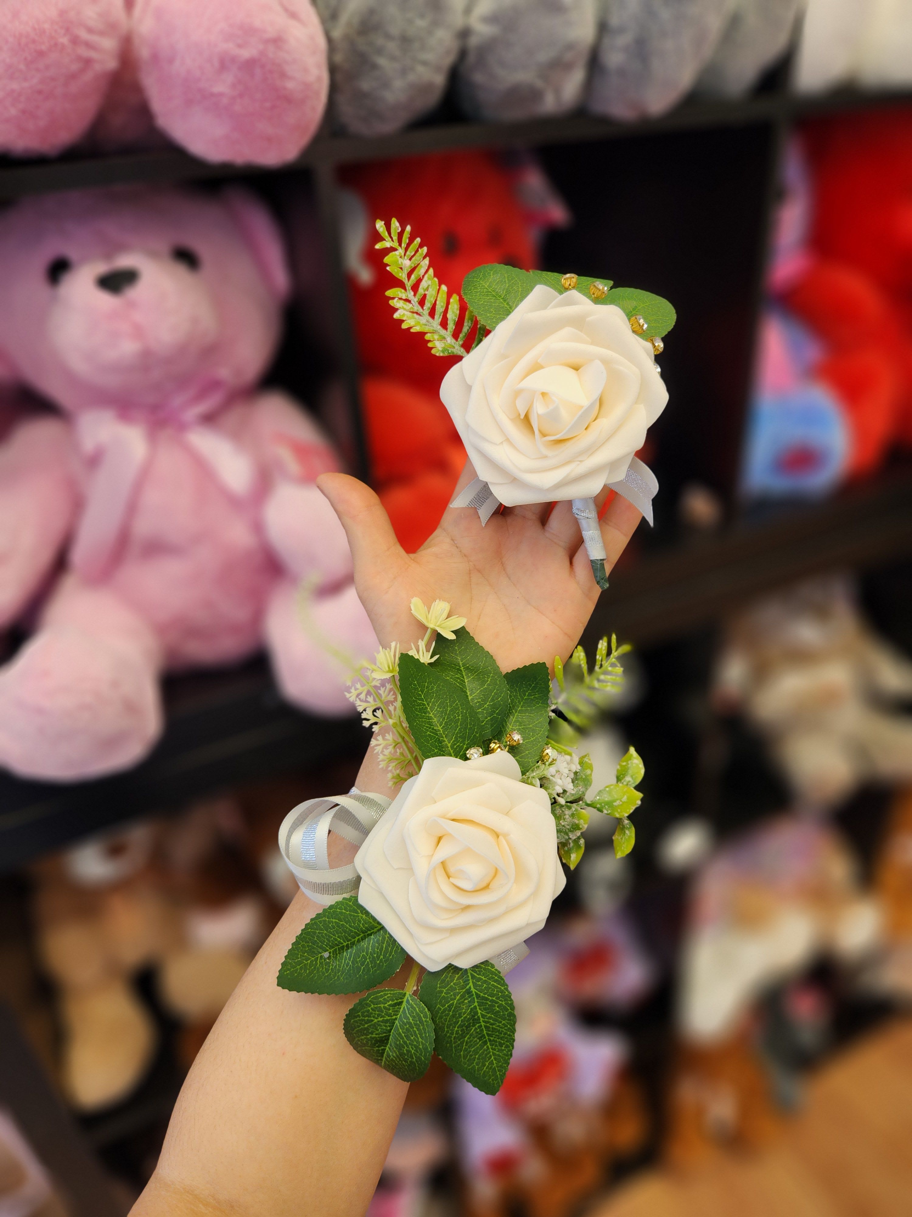 Two white rose corsages with ribbon and greenery held in a hand