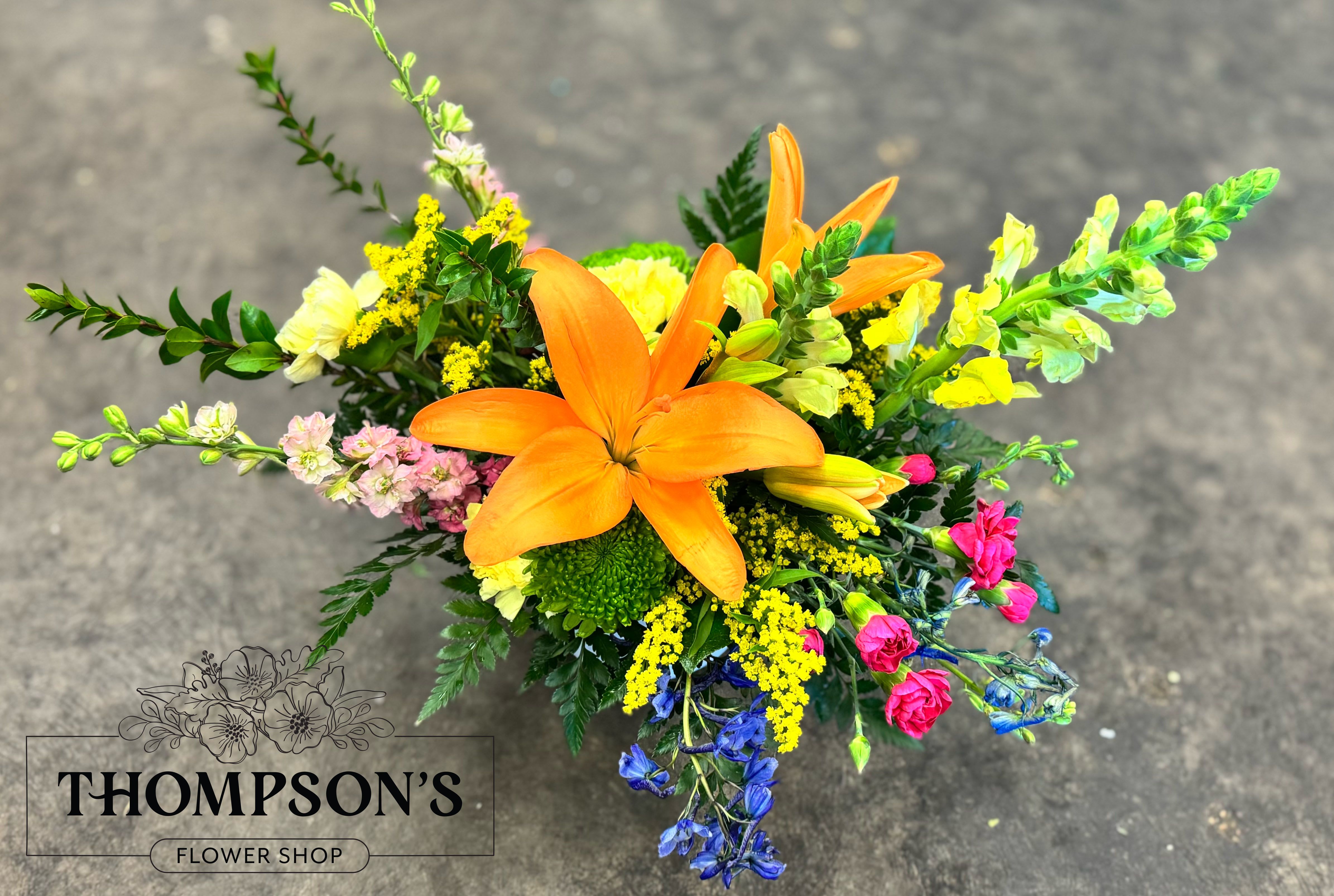 Dear Mama - Designed to honor the love that shows up in a thousand quiet ways, Dear Mama is a heartfelt expression of appreciation. Centered around a striking orange lily and surrounded by vibrant seasonal blooms in warm, uplifting tones, this arrangement feels both bold and deeply meaningful. Thoughtfully arranged in a modern ceramic cylinder, it’s a beautiful way to celebrate everything Mom is and everything she gives. Available exclusively for Mother’s Day week.