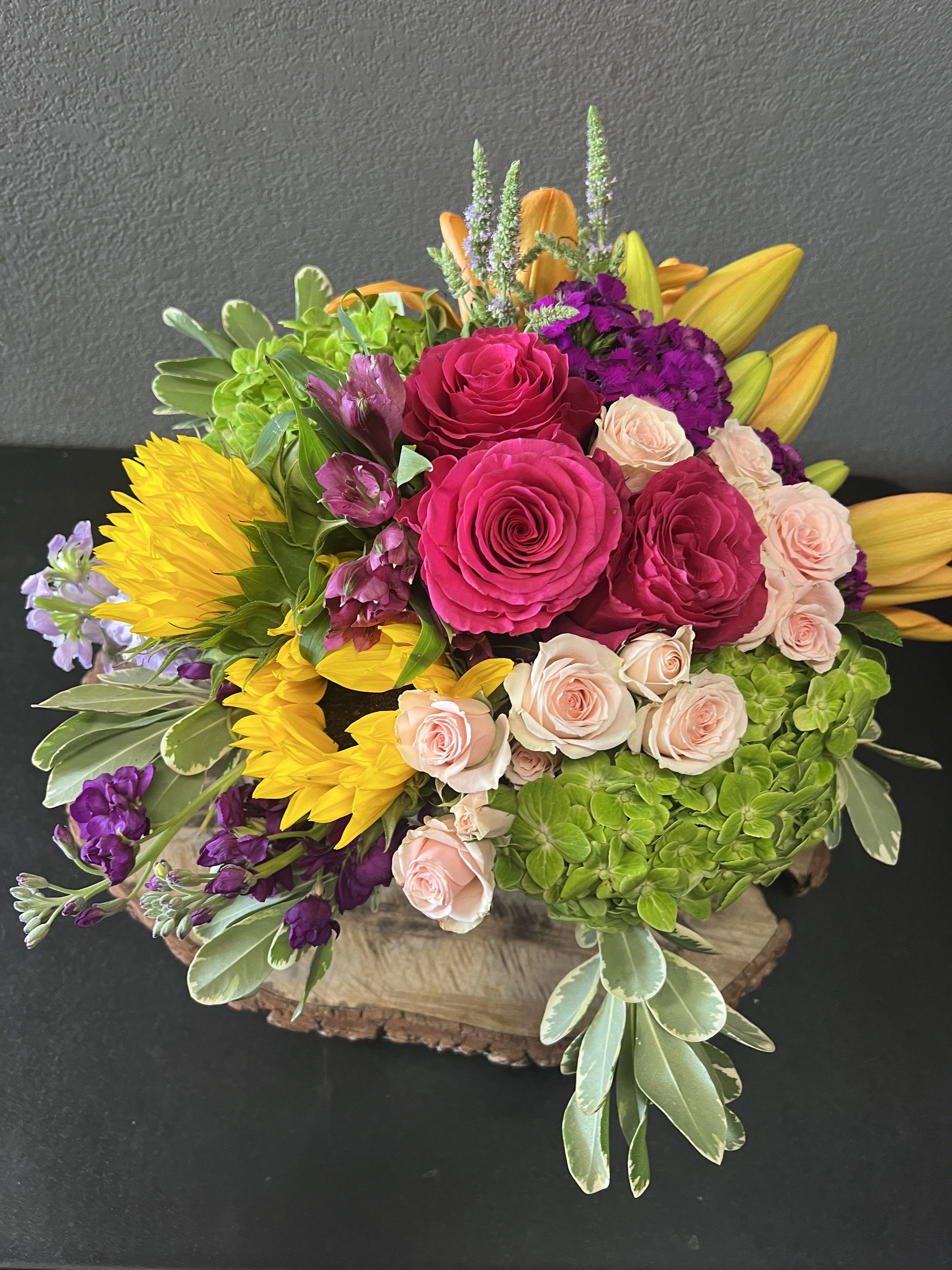 Bright mixed bouquet with roses, sunflowers, lilies, and hydrangea in a wooden base