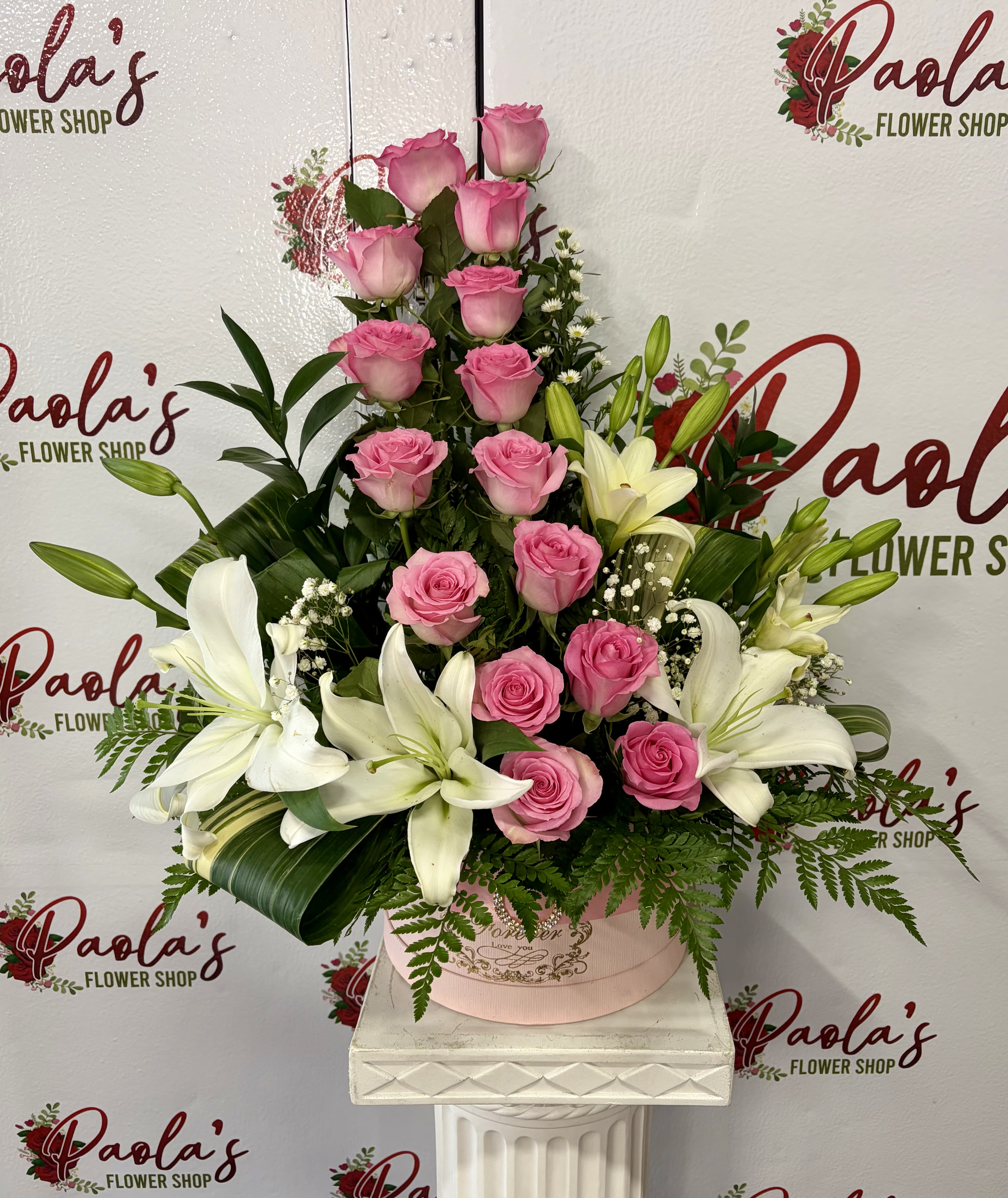    Rosy Lily Bloom Box - A graceful and elevated design that speaks pure elegance. The Rose Lily Bloom Box features a stunning vertical arrangement of soft pink roses paired with fresh white lilies, accented with delicate fillers and lush greenery. Designed in a premium hat box, this piece brings height, beauty, and sophistication to any special moment.  Perfect for Mother’s Day, anniversaries, or meaningful celebrations, this arrangement is made to stand out and leave a lasting impression. Includes:  * Pink roses * White lilies * Baby’s breath &amp; accent florals * Premium hat box container * Fresh greenery  Style: Tall, elegant, and modern Perfect For: Mother’s Day, birthdays, or a luxury floral gift