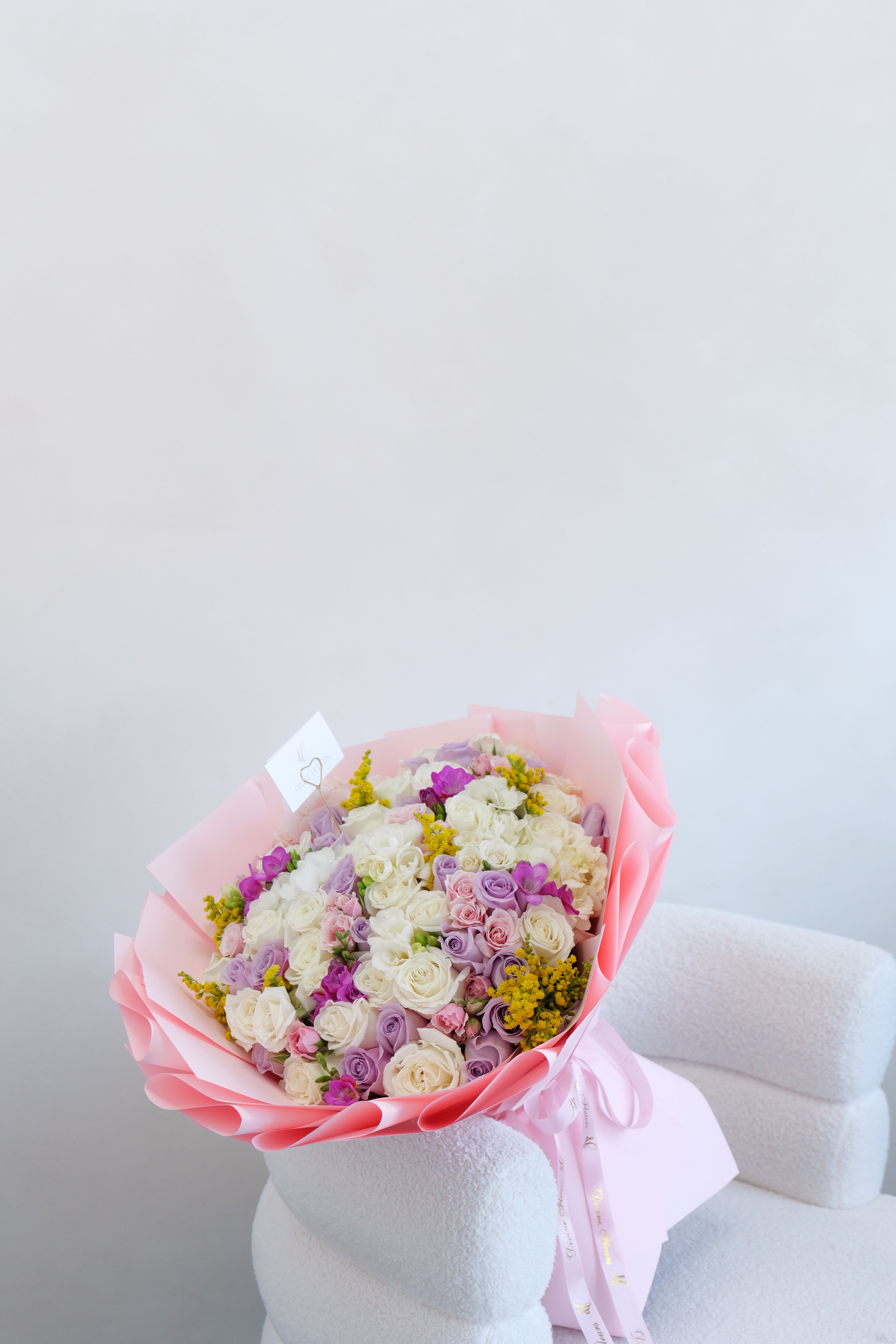Rosie - A cute and charming bouquet filled with soft, pastel blooms in creamy whites, blush pinks, and gentle lavender tones. Designed with fresh roses and delicate seasonal flowers, it has a light, playful feel while still looking elegant and pretty. Wrapped in soft blush paper and finished with flowing ribbons, this bouquet is perfect for sweet moments, thoughtful gifts, or simply making someone smile.  Available in: Standard | Deluxe | Premium Pictured: Deluxe size