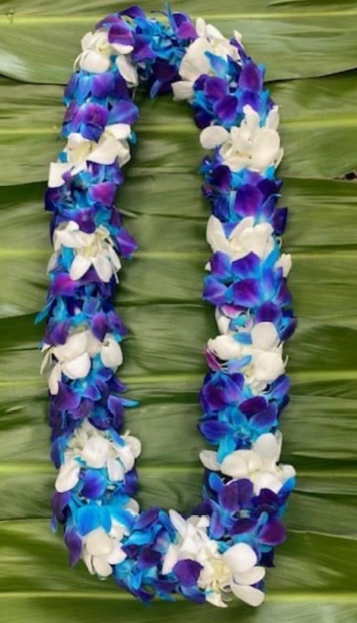 Purple, blue, and white flower lei on a green leaf background