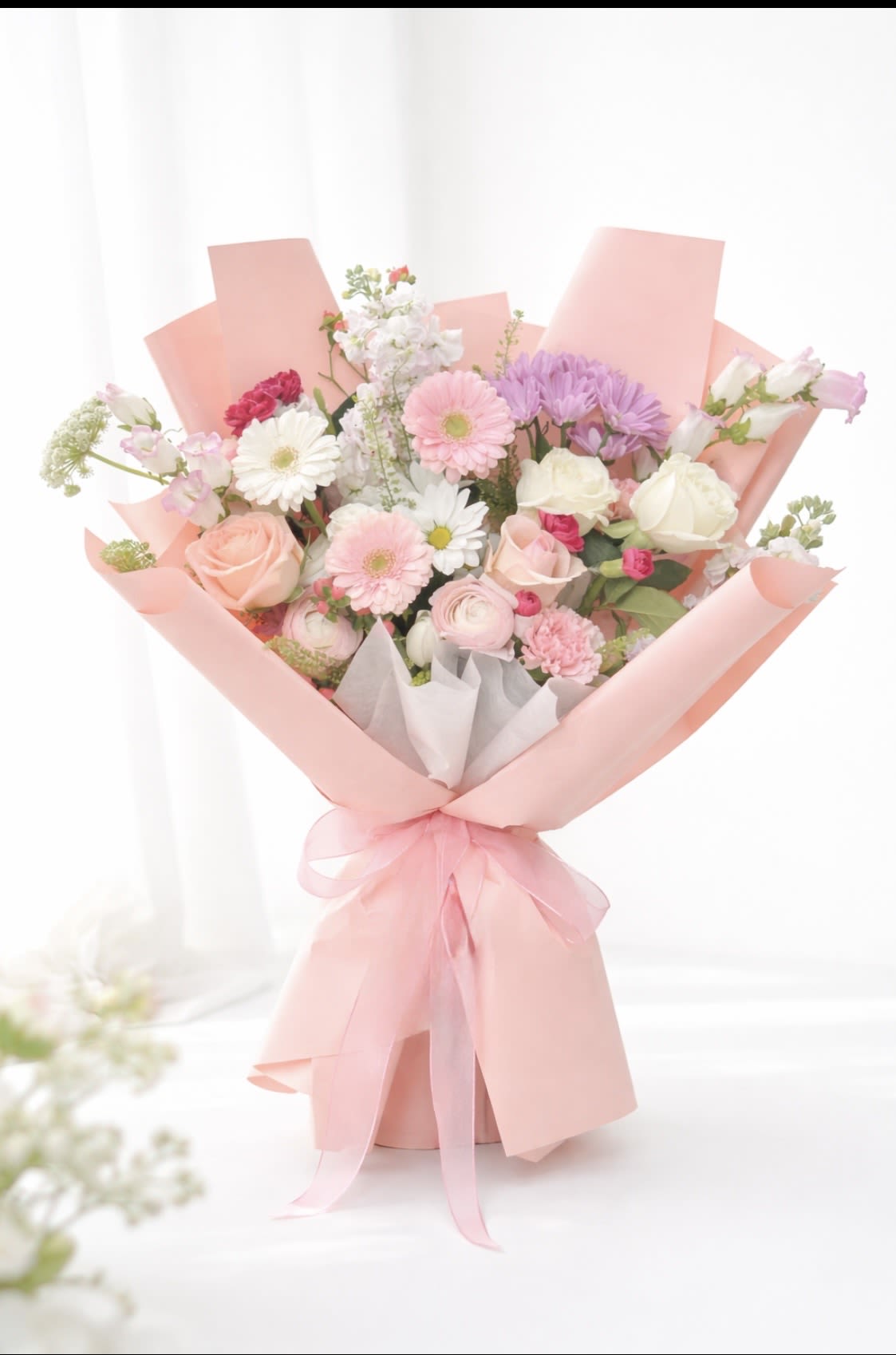 Sweet Unique - Soft pink roses, pale lavender accents, and creamy white blooms come together in a rounded hand-tied bouquet that reads like a whisper of spring - perfect as a birthday bouquet, anniversary flowers, or a cheerful spring gift. The mix of roses, gerbera daisies, carnations, alstroemeria and small daisy-like accents creates a soft, romantic impression that will make the person you're thinking of feel cherished and celebrated.  This arrangement is wrapped in pink wrapping paper with white tissue and tied with a pink ribbon, giving it a polished, gift-ready look the moment it arrives. The bouquet includes airy filler stems that add light texture and depth, keeping the silhouette fresh and full without feeling heavy. Its pastel palette of pink, white and lavender blends well with many interiors and outfits, making it an easy choice when you want a gentle, joyful floral statement.  Send this to mark a milestone or simply to brighten a day; it reads as both intimate and celebratory so it suits partners, close friends, or family members. For best enjoyment, place in clean water on arrival and trim stems slightly to help the flowers open and last longer.
