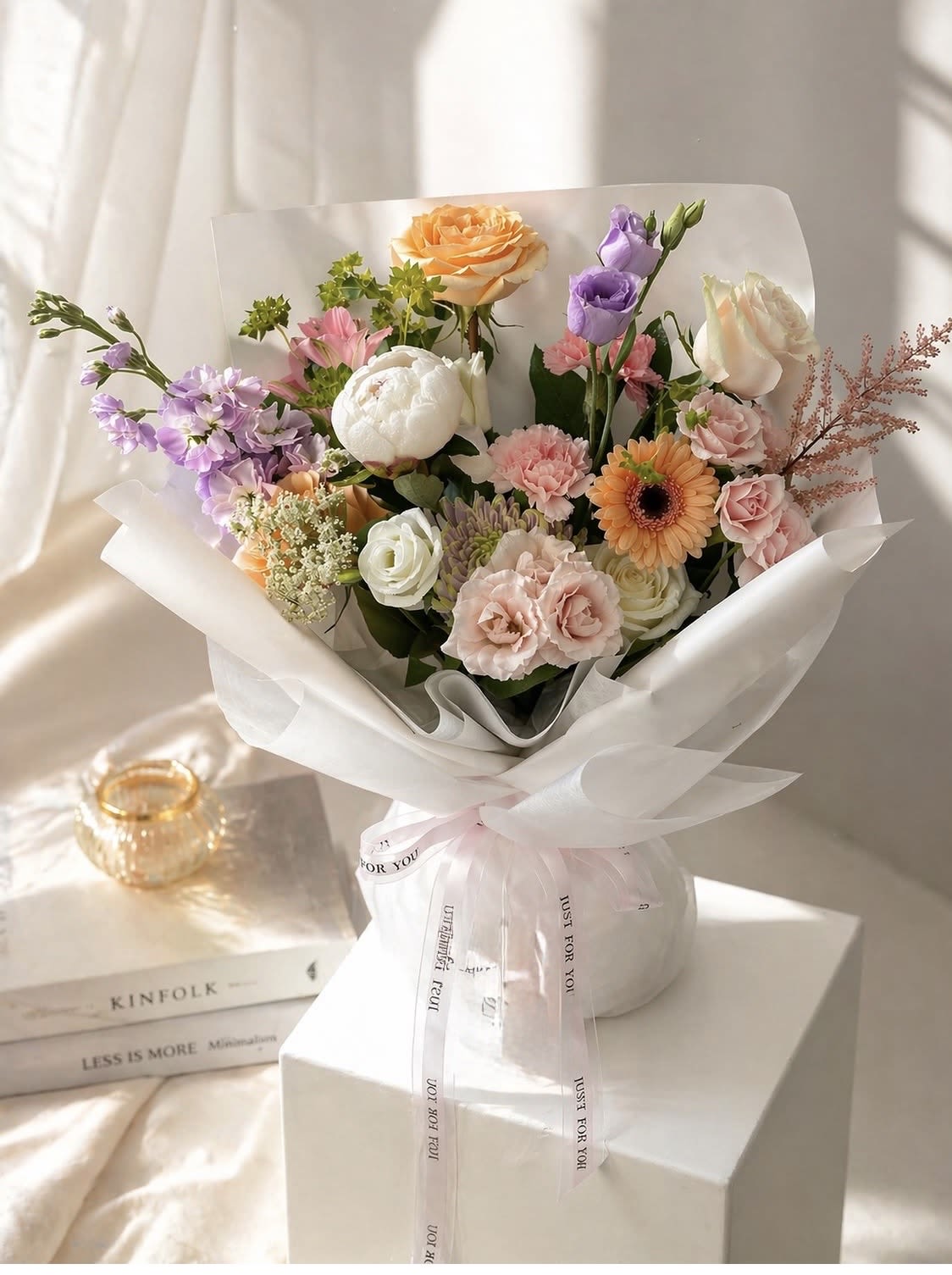 Beautiful Wednesday - Soft pastels of pink, white, lavender and peach create a tender, romantic statement in this hand-tied bouquet - perfect as a birthday bouquet, anniversary flowers, or a just-because surprise to make someone feel truly cherished. The rounded, airy arrangement reads fresh and feminine at a glance; the person you're thinking of will feel gently celebrated the moment they see the soft color harmony and delicate textures.  This bouquet features roses, lisianthus, carnations and a single gerbera daisy interspersed with light filler accents for movement and depth. It's presented in a clean white paper wrap tied with a pale satin ribbon, or optionally arranged in a simple white vase for an easy, gift-ready display. The mix of bloom shapes - ruffled carnations, classic roses, cup-shaped lisianthus and the bold gerbera center - offers visual contrast and a soft, fragrant presence.  Suited to springtime celebrations or any moment you want to brighten, this arrangement reads as both elegant and approachable - the kind of bouquet that makes someone feel seen and appreciated. Choose wrap for a hand-delivered touch or the white vase for immediate tabletop charm; care is simple-fresh water and a fresh cut every few days will keep the blooms looking their best.
