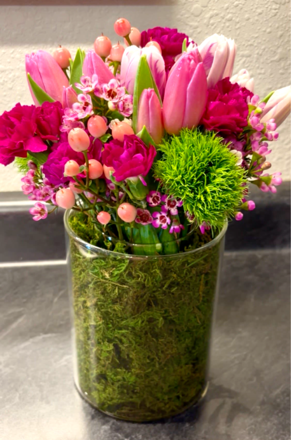 Pink tulips and magenta flowers arranged in a clear glass vase