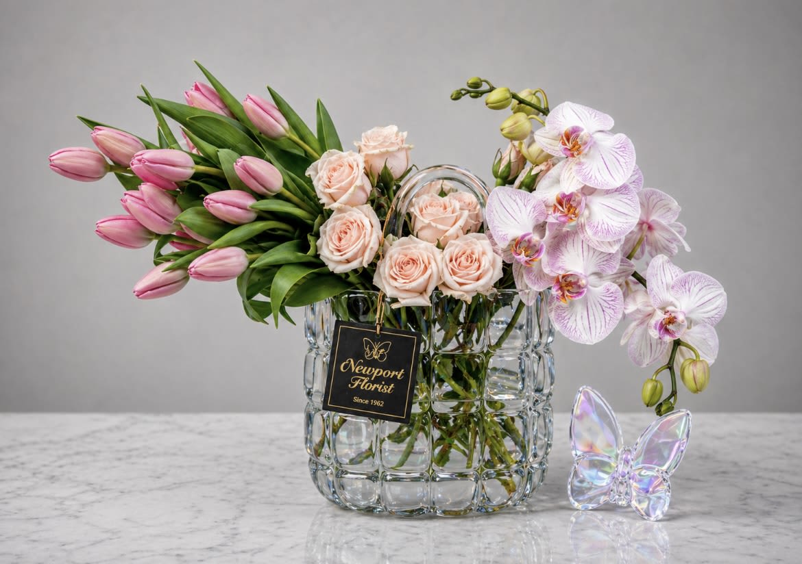 Tulip &amp; Orchids Harmony in Crystal Basket NF-Y44 - A sweeping cluster of pink tulips meets pale blush roses and cascading white-and-lavender Phalaenopsis orchids in this flower arrangement-perfect as a birthday bouquet, Mother's Day gift, or a romantic surprise. The soft, mixed pinks and greens create a gentle, uplifting presence that says "thinking of you" or "congratulations" without shouting, so the person you care about will feel seen and celebrated.  Arranged in a clear, textured glass vase with an iridescent butterfly ornament and a florist tag, the design balances movement and elegance: tulips provide lively sweep, spray roses add delicate texture, and the orchids lend a graceful drape. The palette of pink, white and green reads fresh for spring but remains appropriate year-round for occasions like retirement, get well, housewarming, graduation, or just because.  This arrangement arrives ready to display; its compact, contemporary vase fits on a bedside table, mantel, or kitchen island to brighten daily life. For longer enjoyment, refresh water every few days and trim stems at an angle before re-setting-an easy way to help her feel genuinely celebrated.
