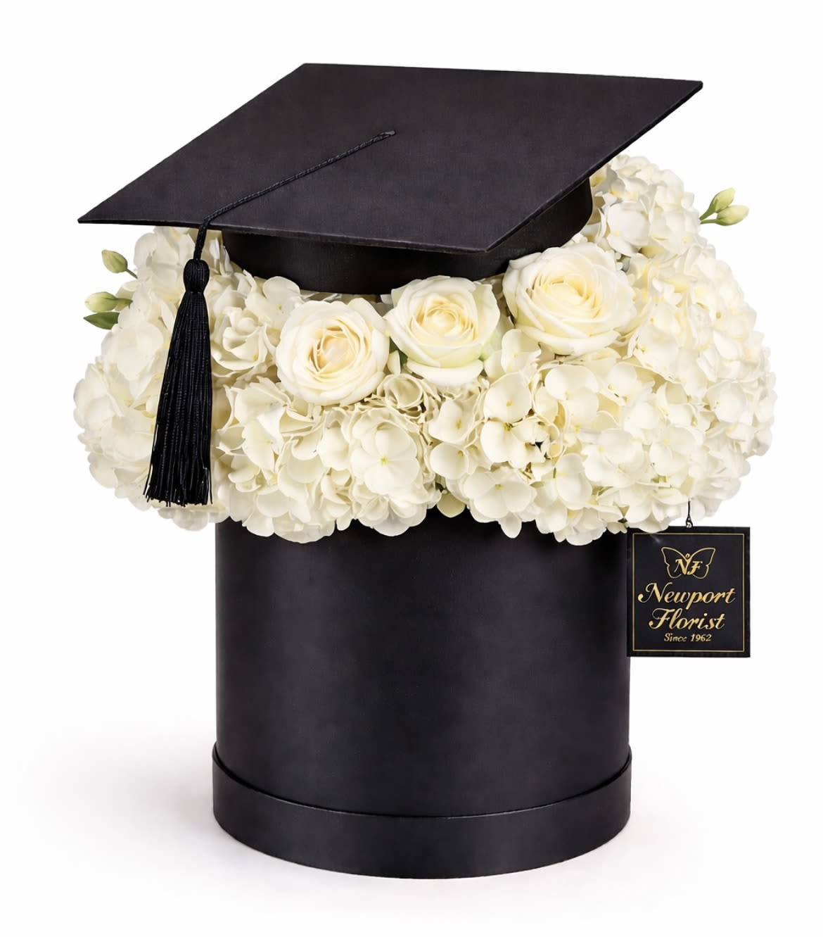 Ivory Graduation Elegance NF-Y47 - White roses and clustered white hydrangeas are artfully arranged in a sleek black graduation cap box, creating a crisp black-and-white graduation bouquet that's both formal and celebratory. Designed specifically as a graduation gift, the compact, rounded floral mass reads as polished and intentional-perfect for the graduate who deserves a classic, memorable moment. The decorative tassel and branded tag add an extra touch of ceremony and provenance, so the recipient will feel truly recognized.  This arrangement features pure white roses paired with lush white hydrangea blooms set low in a cylindrical hat box shaped like a graduation cap. The monochrome palette emphasizes texture-the velvety rose petals against the fluffy hydrangea clusters-while the compact size makes it easy to carry and display on a mantle, dorm shelf, or desktop. The included tassel and graduation cap styling make this a ready-to-gift piece that signals accomplishment and pride.  Ideal for graduates, proud family members, or faculty presentations, this keepsake-style box bouquet sends a clear message: congratulations and well done. Because it arrives pre-arranged in its decorative hat box, it's an effortless presentation-ready gift; keep the flowers in a cool spot and refresh water if supplied to extend their life.