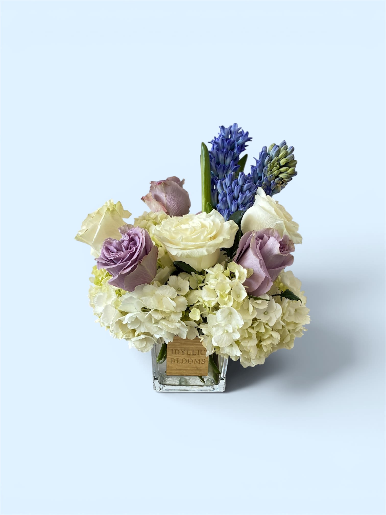 Lavender love  - Lavender love is a delicate blend of creamy white hydrangeas, elegant ivory roses, and muted lavender roses, accented with fragrant blue hyacinth for a touch of charm. Designed in a modern glass cube, this arrangement offers a calming, refined look that’s perfect for expressing love, appreciation, or quiet comfort.
